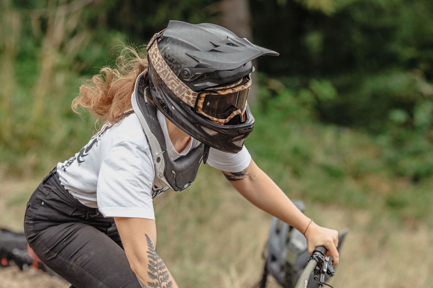 Mountain biker wearing protective helmet and gear rides trail through nature setting in sunny conditions.