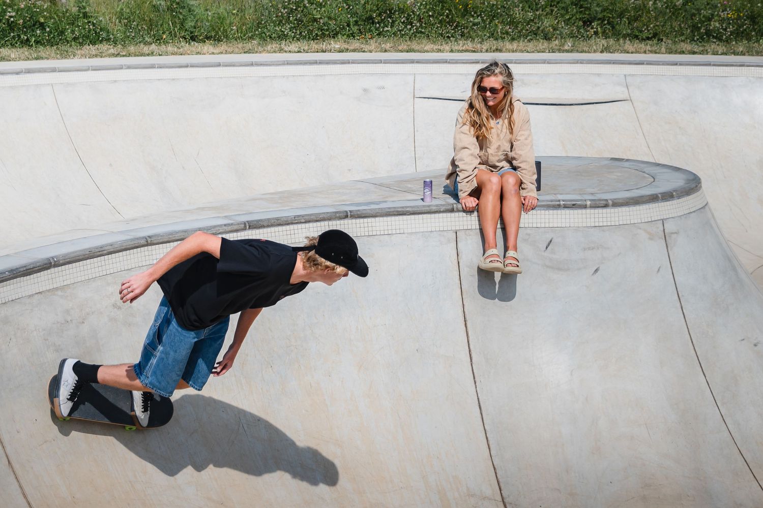 Two skateboarders practice tricks at a concrete skate park on a sunny day.