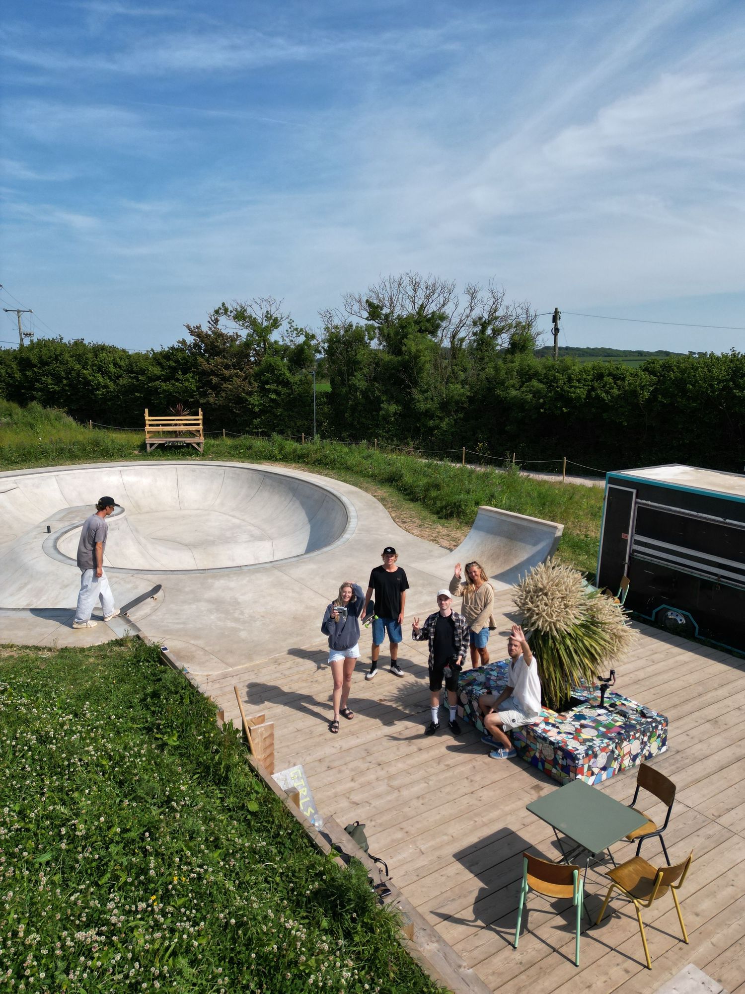 A group of photographers gathered at outdoor skate park with concrete bowl and benches on a sunny day.