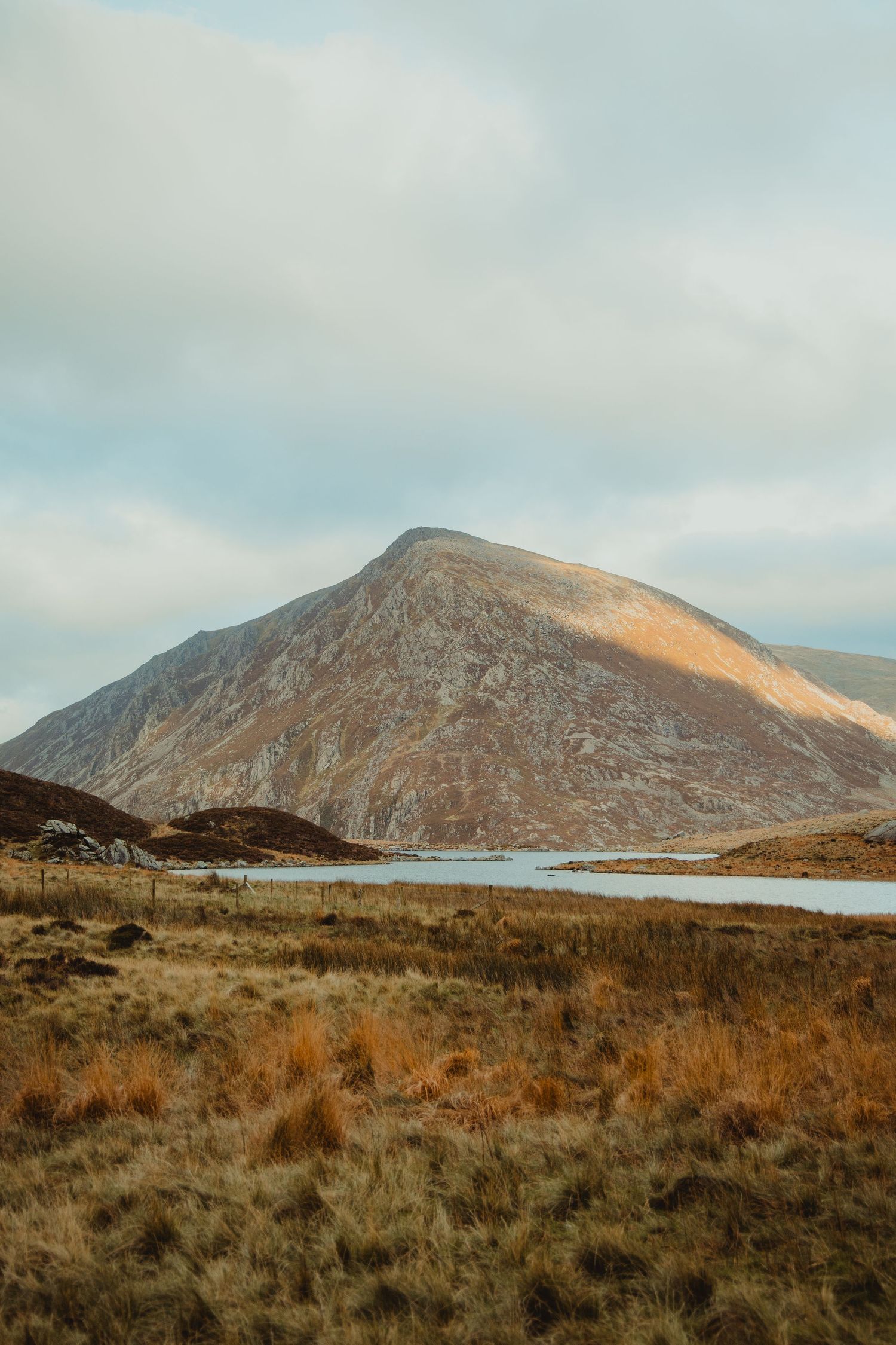 Scenic autumn landscape with a large mountain beside a calm lake under a cloudy sky in Ireland.