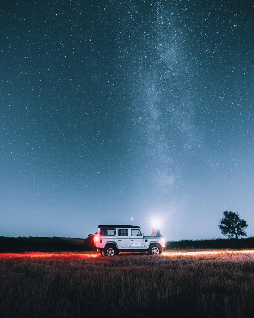 Off-road vehicle parked under starry night sky with Milky Way and red ground lighting creating dramatic scene.