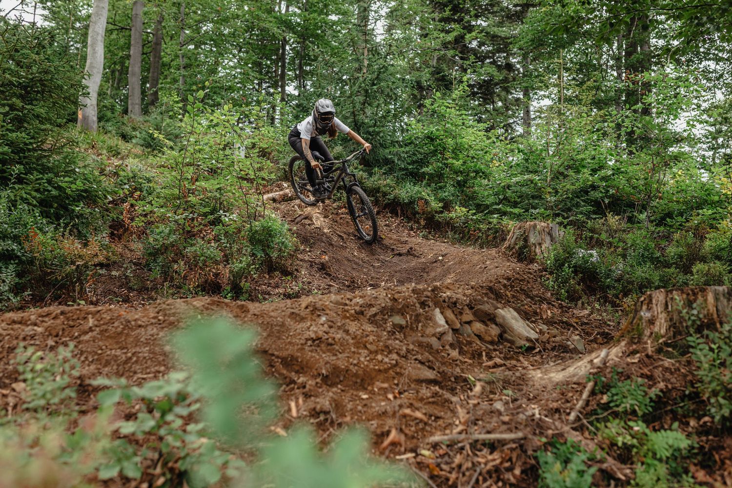 Mountain biker riding downhill on muddy forest trail through green woodland.