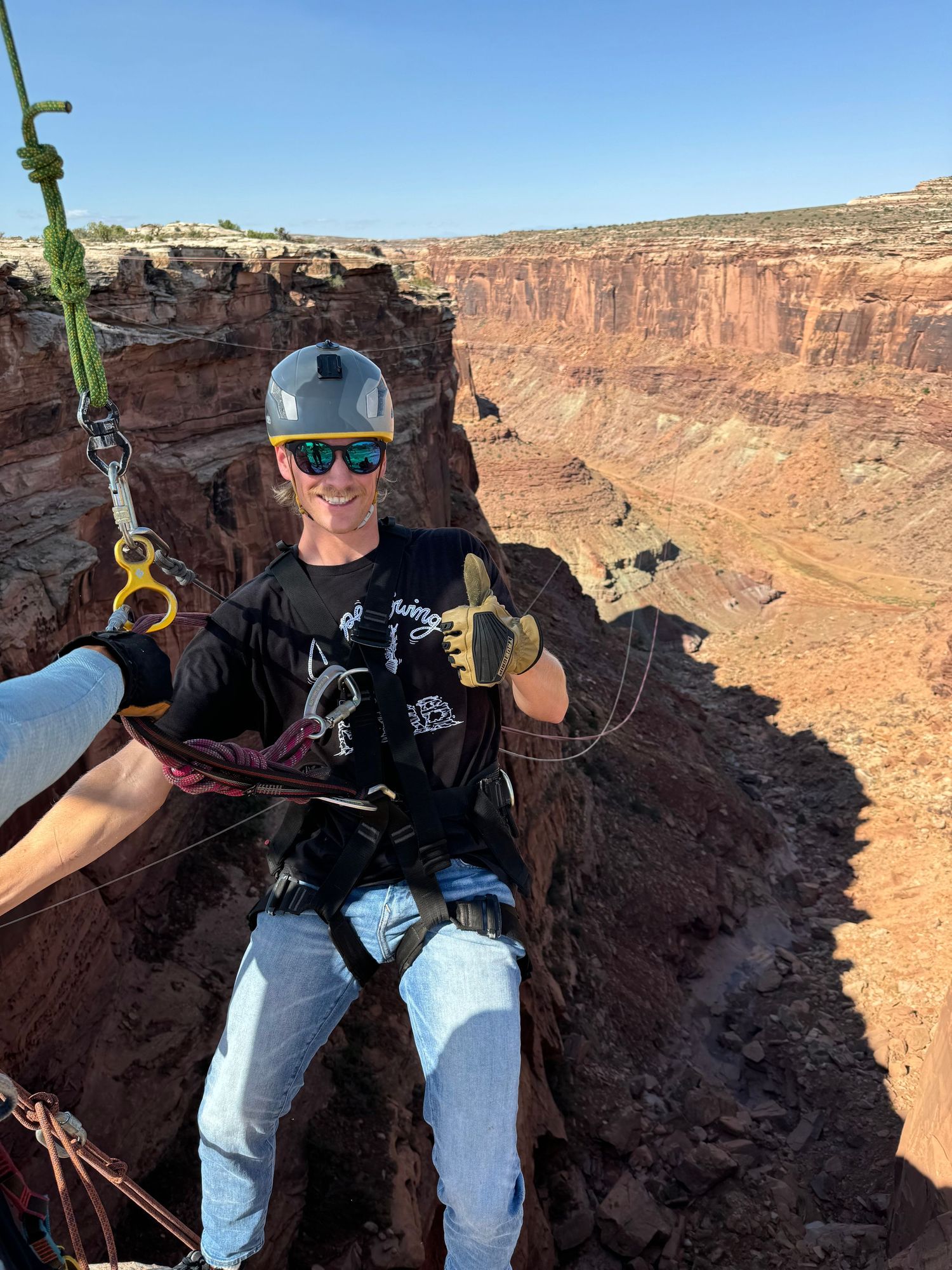 Adventure seeker harnessed for rock climbing poses against dramatic red canyon backdrop.