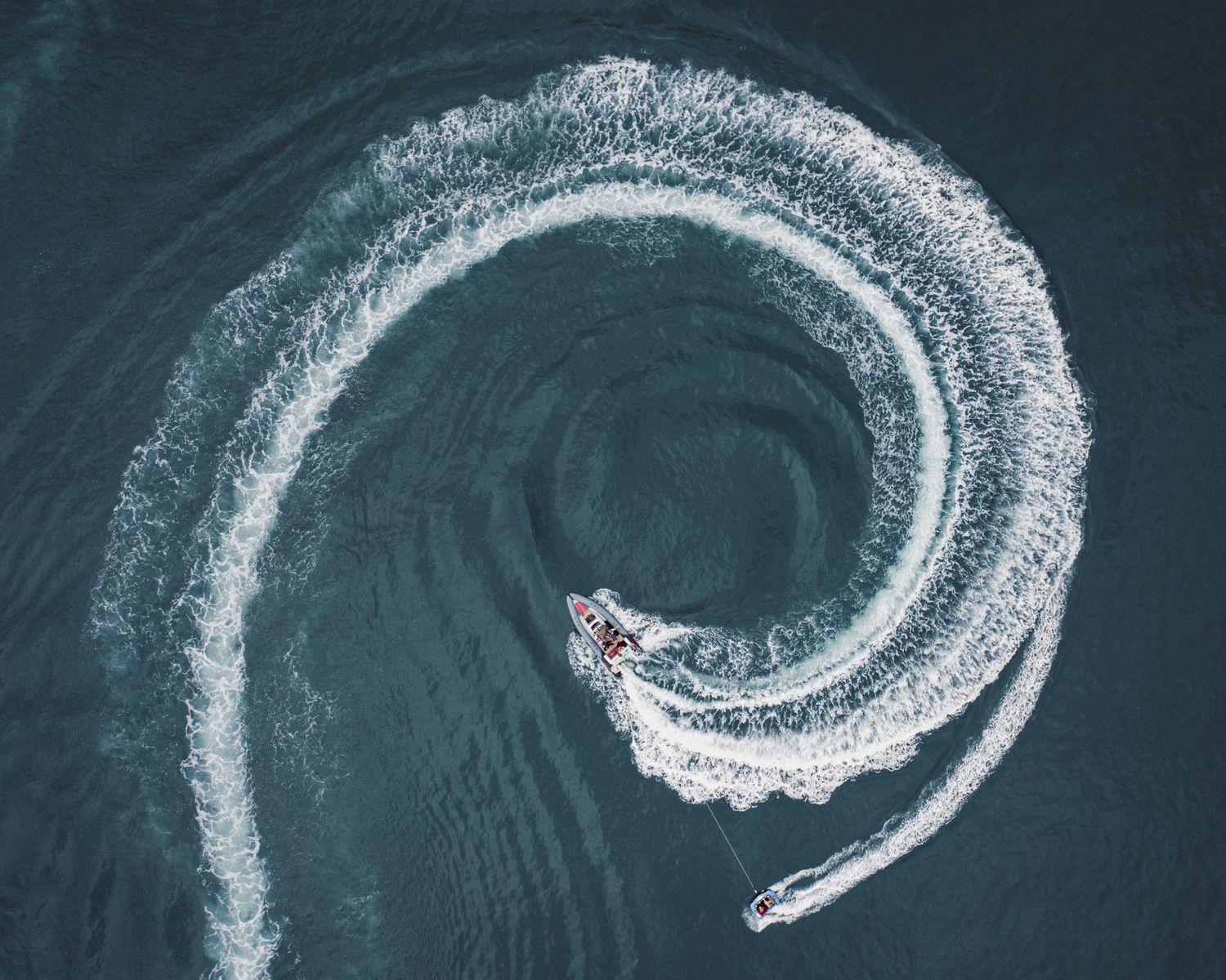 Aerial view of a boat making a perfect spiral pattern in dark blue ocean water with white wake trail.