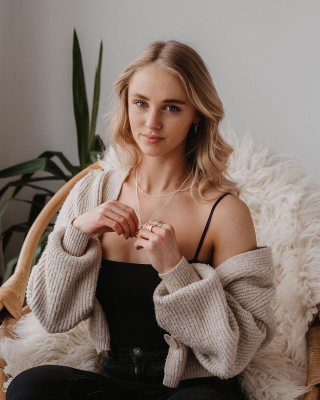 Portrait of someone in a black top and beige cardigan sitting in a cozy chair with tropical plant decor.
