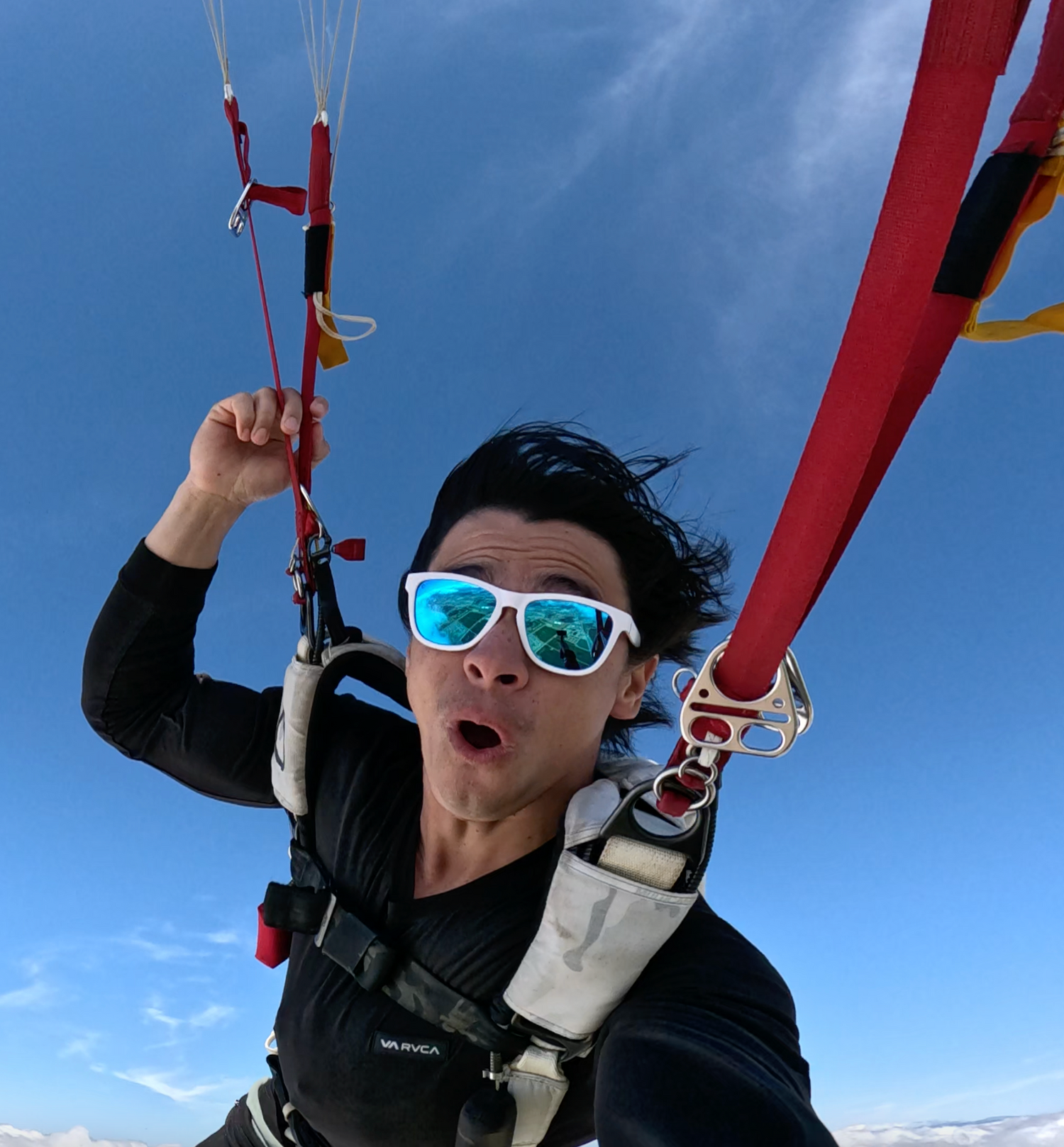 Skydiver in blue sunglasses taking excited selfie during freefall. Part of a UGC campaign.