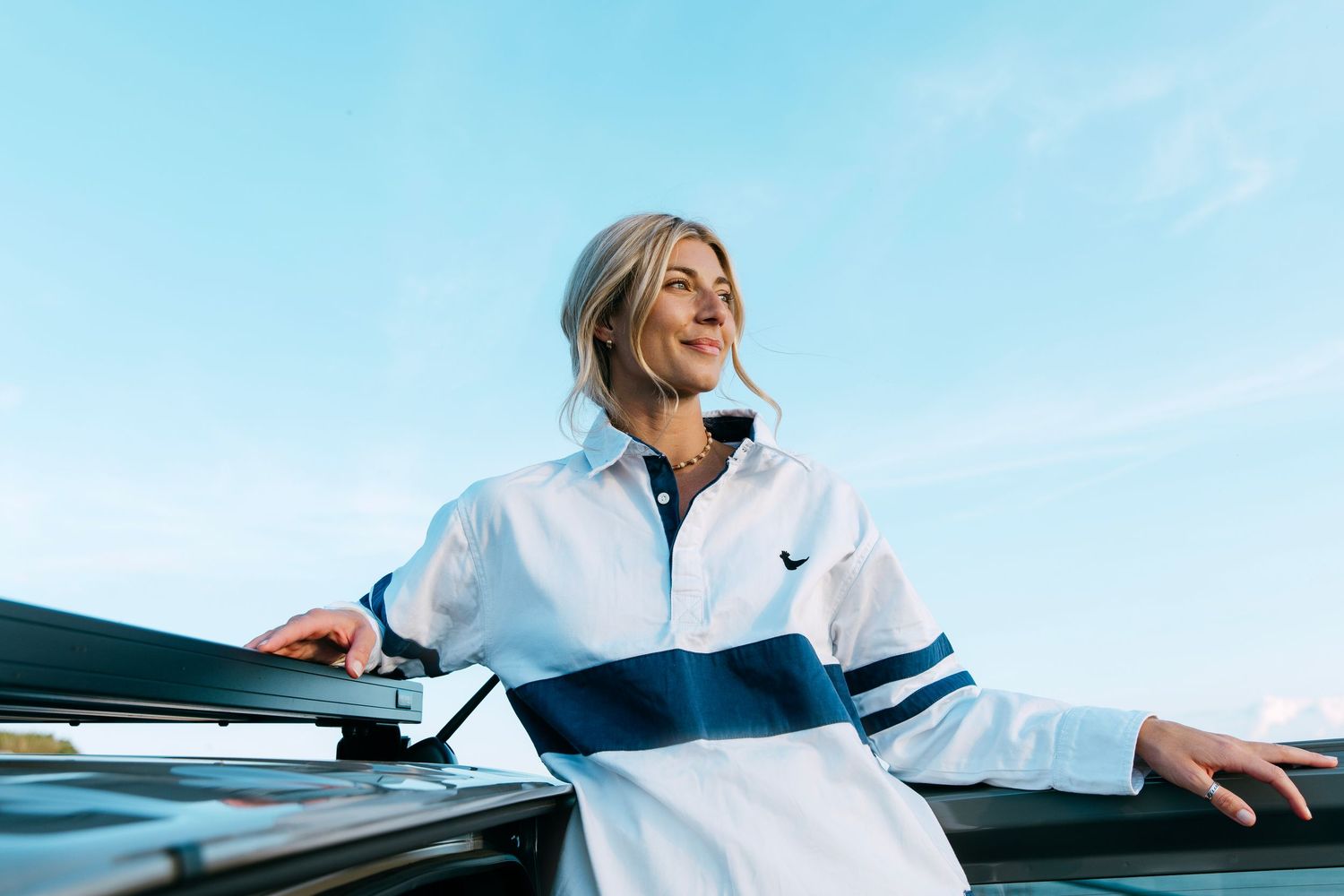 A person in a white jacket leans back and smiles while sitting in a car with blue interior details.
