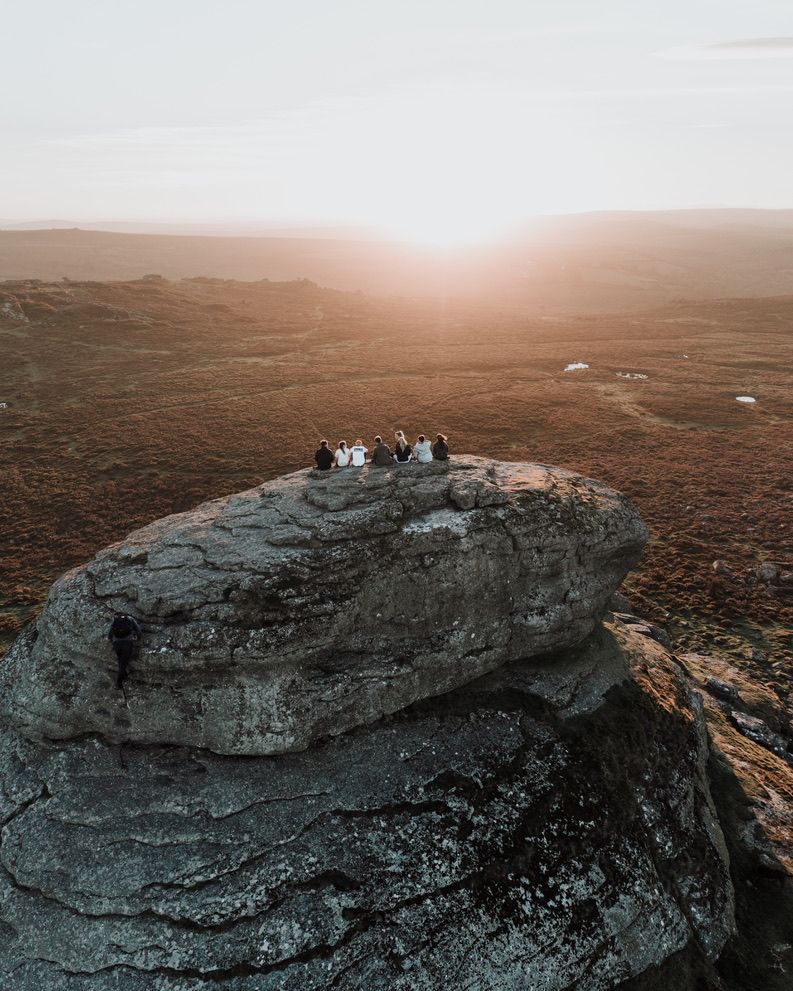 Three dogs sit atop a large gray boulder formation against a misty mountainous landscape at sunset.