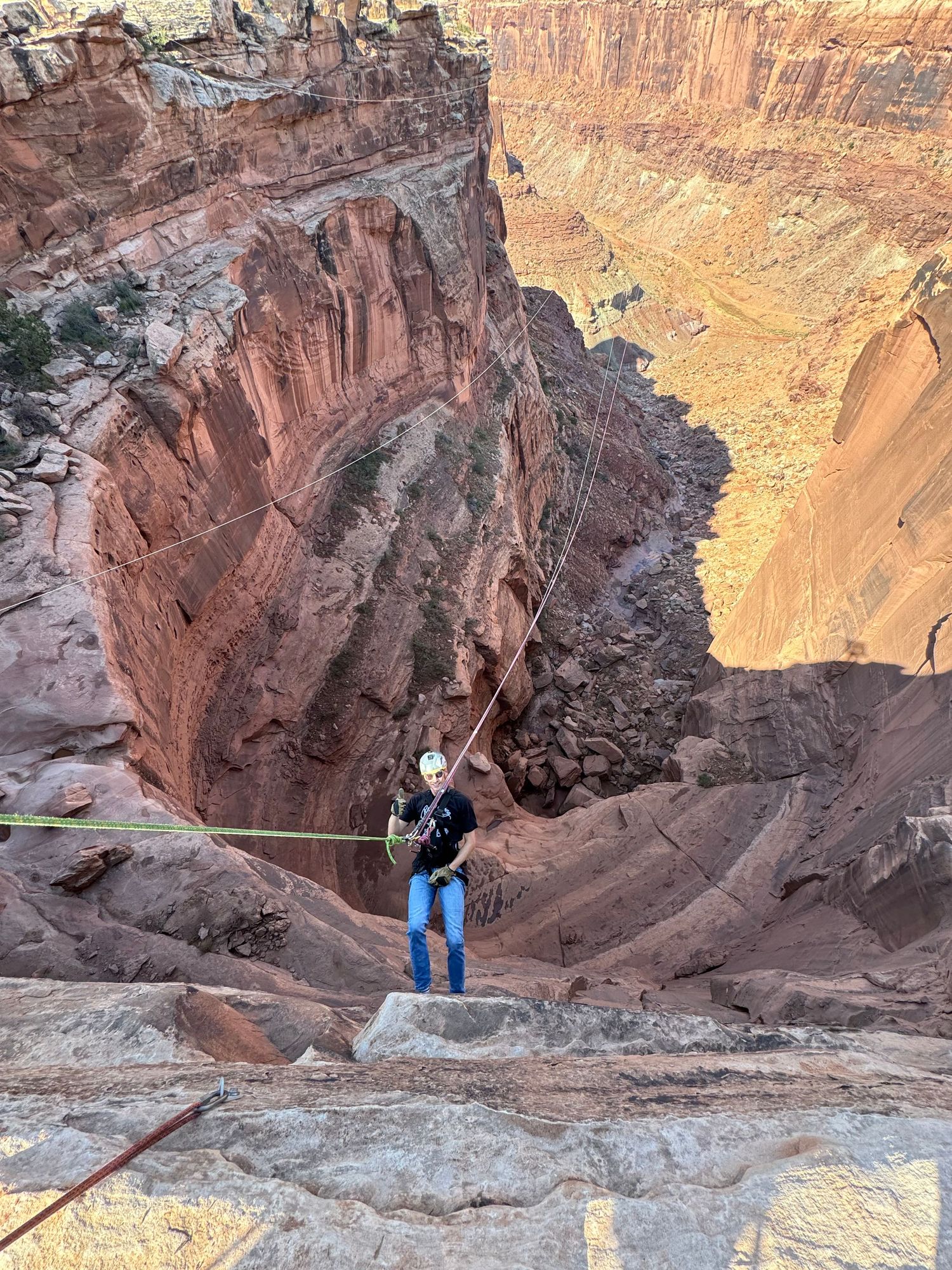 Adventurous climber rappels down steep red rock canyon cliffs at sunset in the American Southwest wilderness.