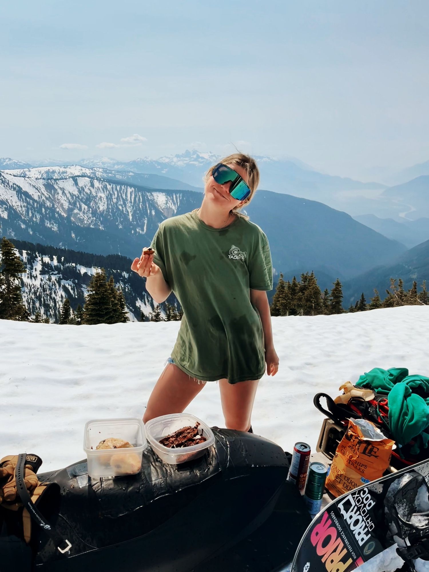 A snow-covered mountain scene with ski and snowboarding gear laid out in front of a person in a green shirt.