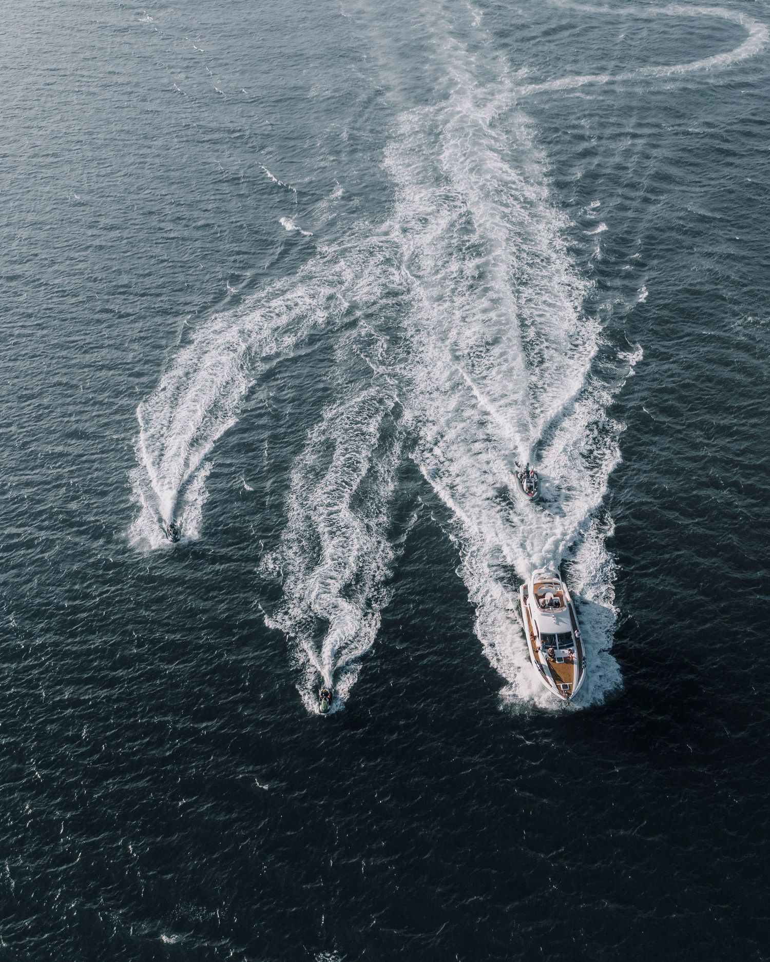 Aerial view of a motorboat creating intricate wake patterns on dark blue ocean water.