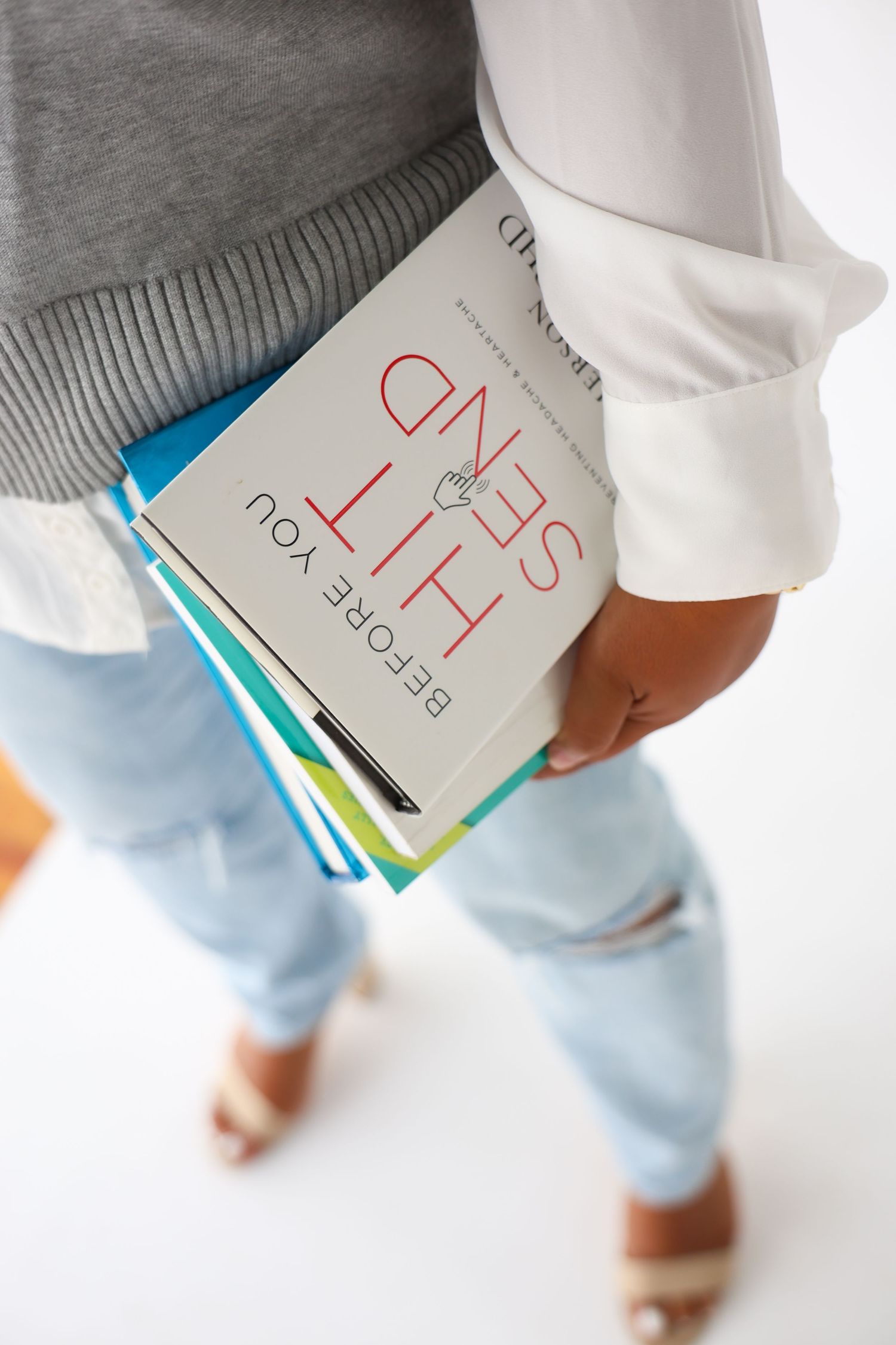 Person holding books including 'Before You Hit Send' while wearing jeans and heels, viewed from above.