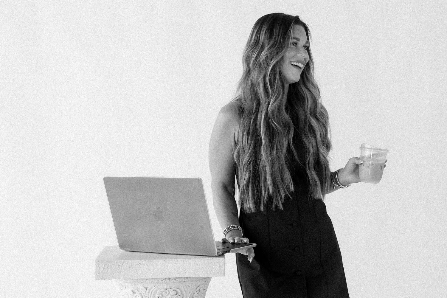 Woman smiling with laptop and glass in black and white photo, casual professional style.