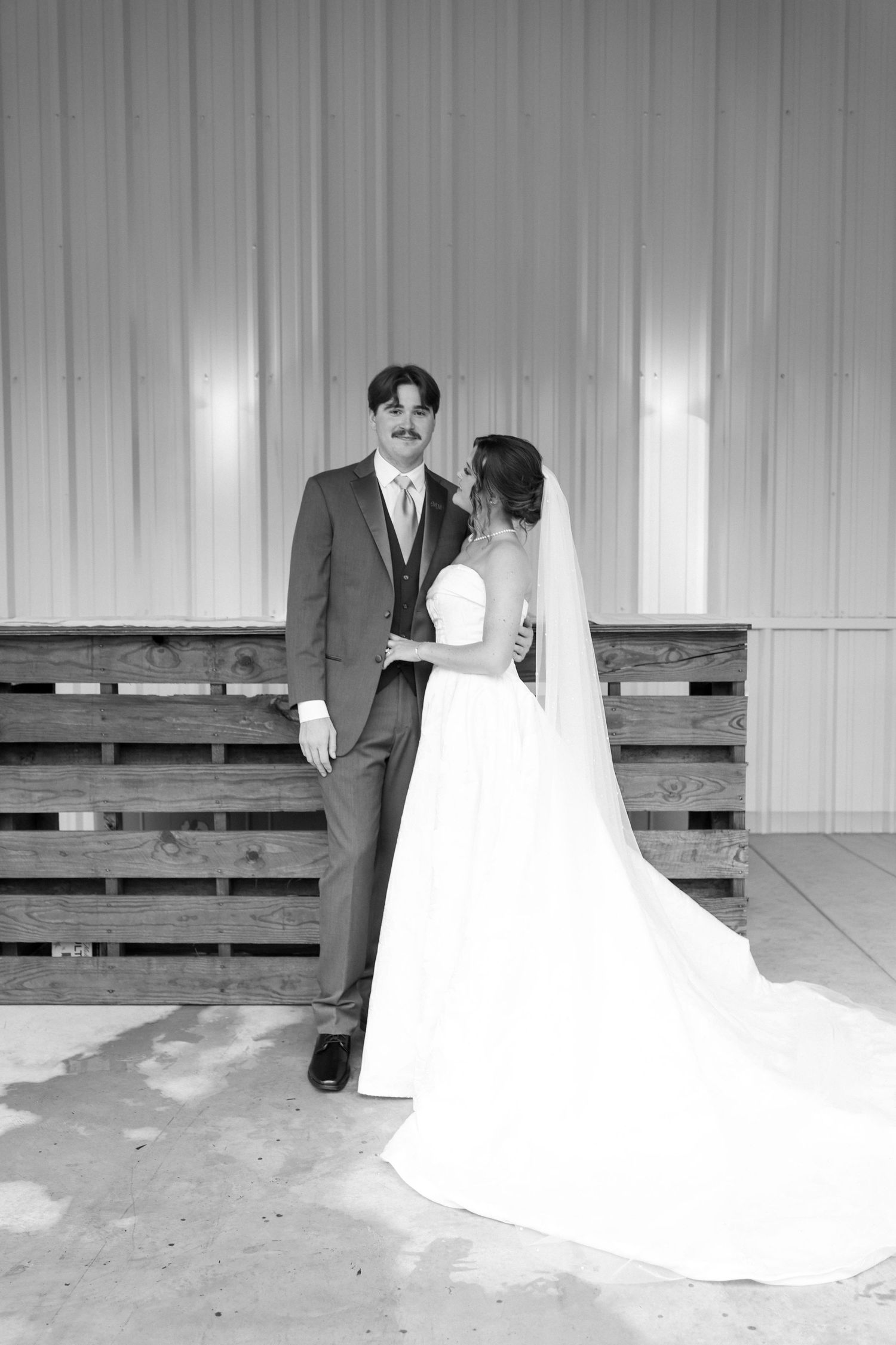 Black and white photo of a bride in a flowing white gown and groom in a suit posing together at a wedding venue.