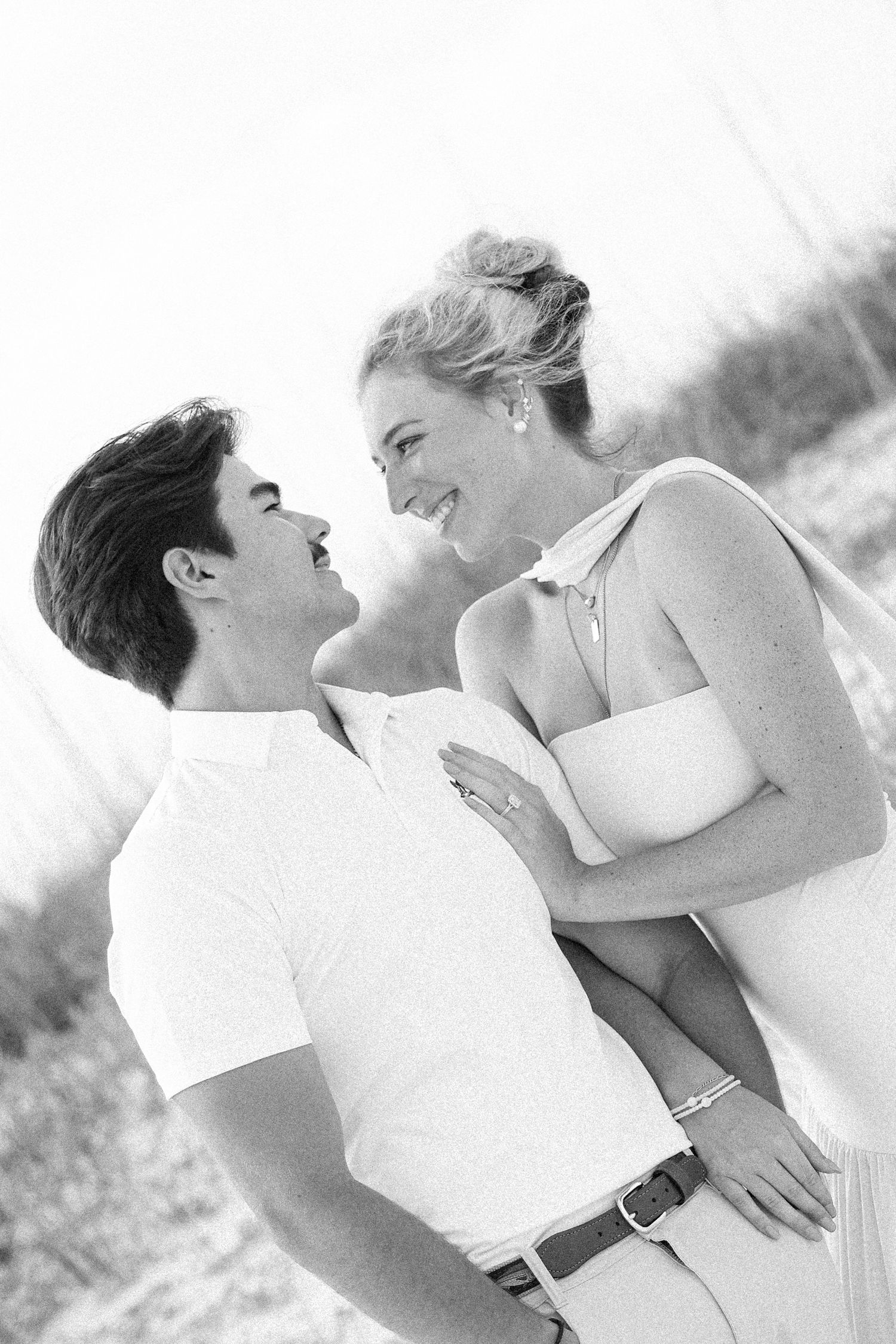 Black and white photo of a happy couple embracing and smiling at each other on a beach.