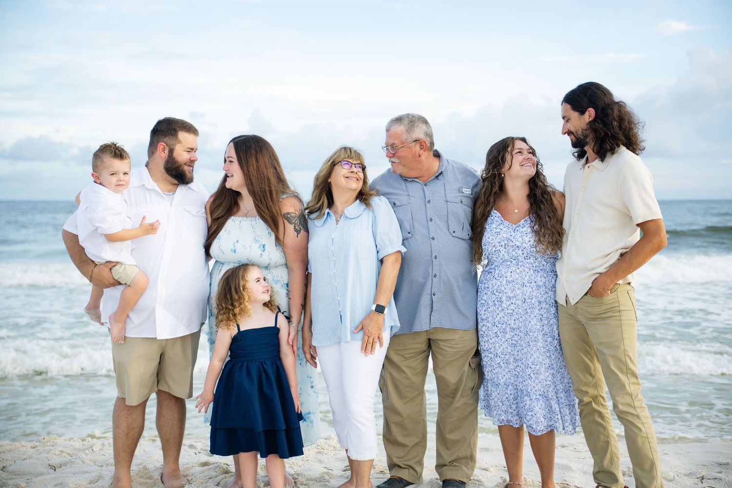 Multi-generational family portrait on a beach, smiling together with ocean waves in the background.