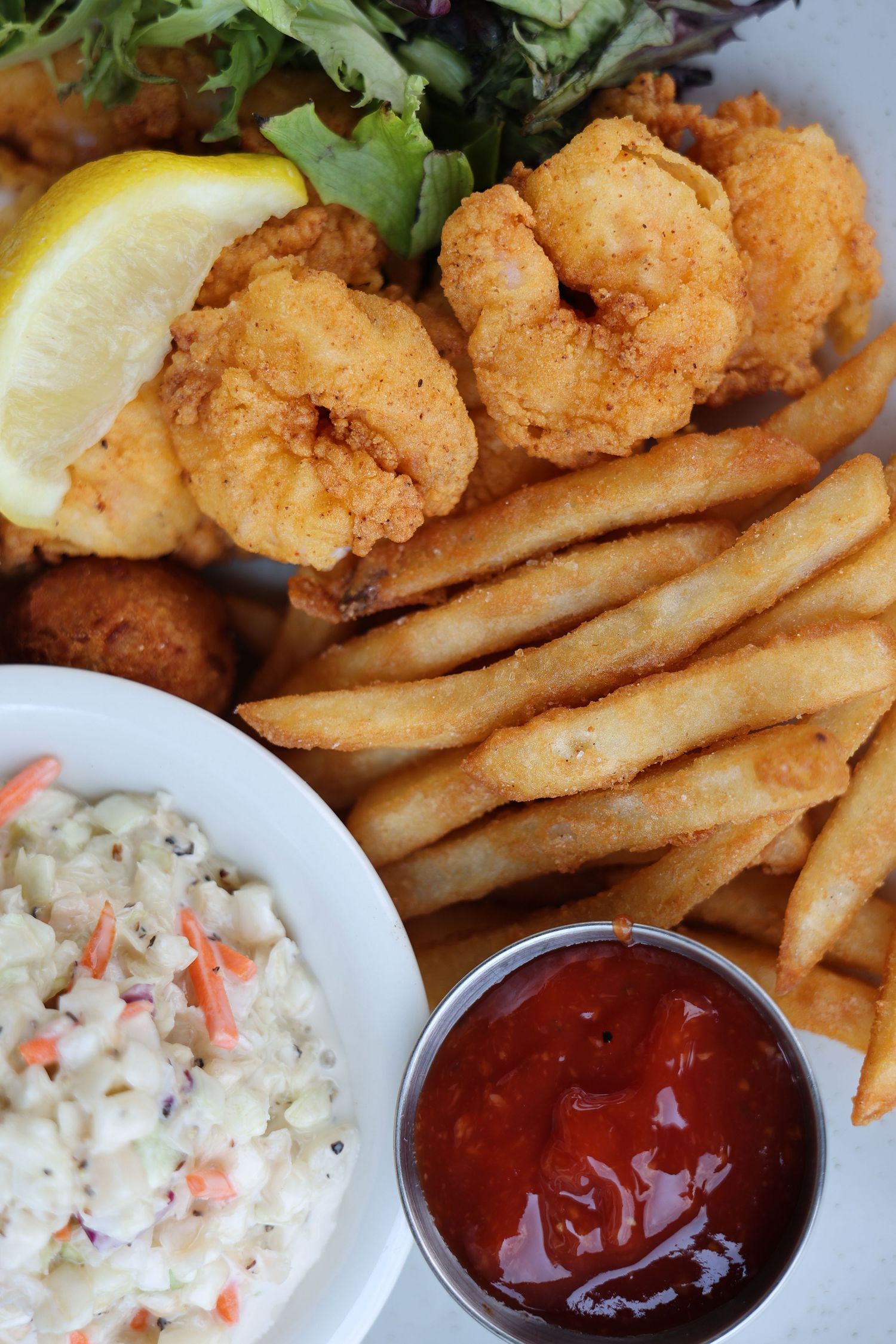 Fried shrimp basket with crispy french fries, coleslaw, cocktail sauce, and a lemon wedge on a white plate.