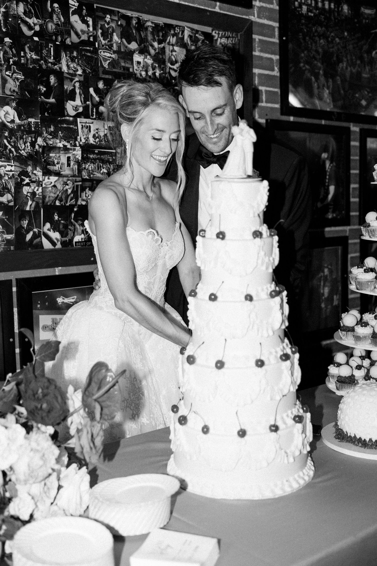 Bride and groom cutting tall five-tier white wedding cake together at reception in black and white photo.