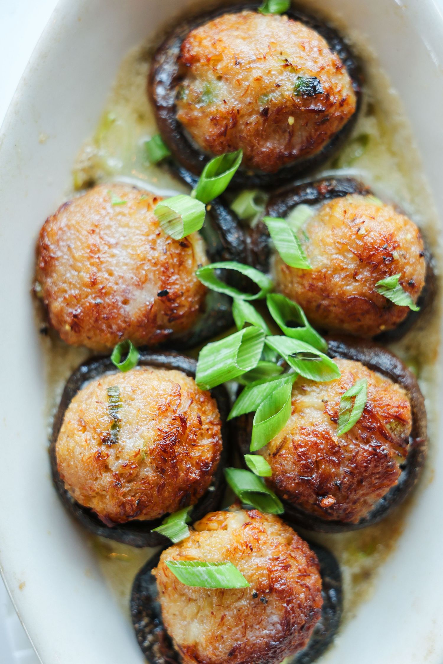 Golden stuffed mushrooms topped with breadcrumbs and fresh green onions in a white baking dish.