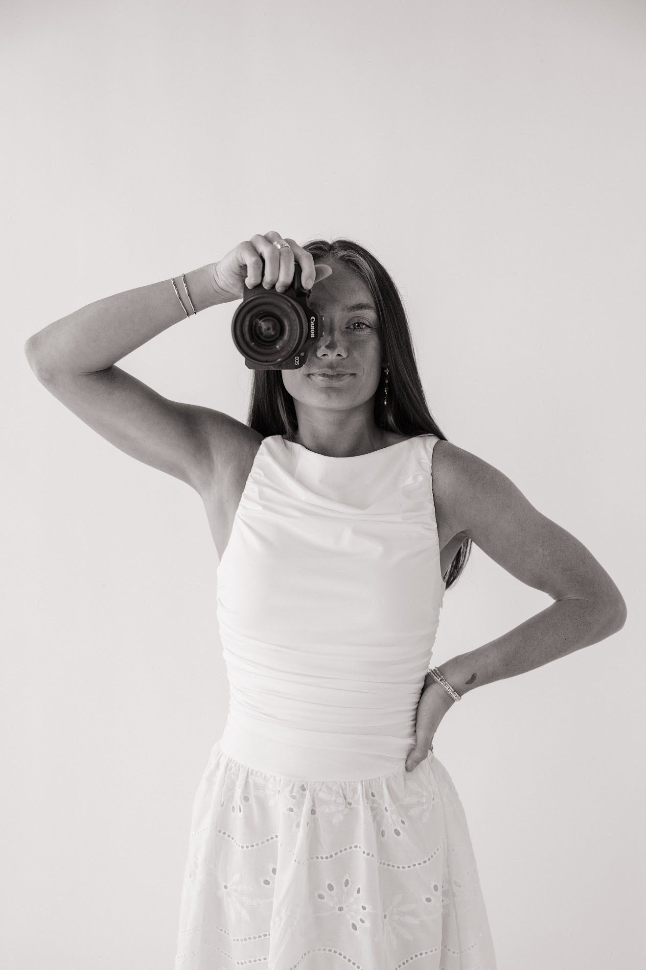 Young woman in white dress holding camera to her face, black and white photo.