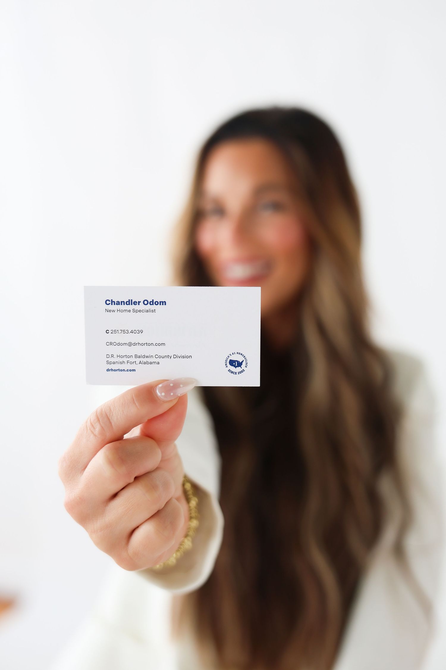 Smiling woman with long hair holding a business card for Chandler Odom, Real Estate Specialist, in Alabama.