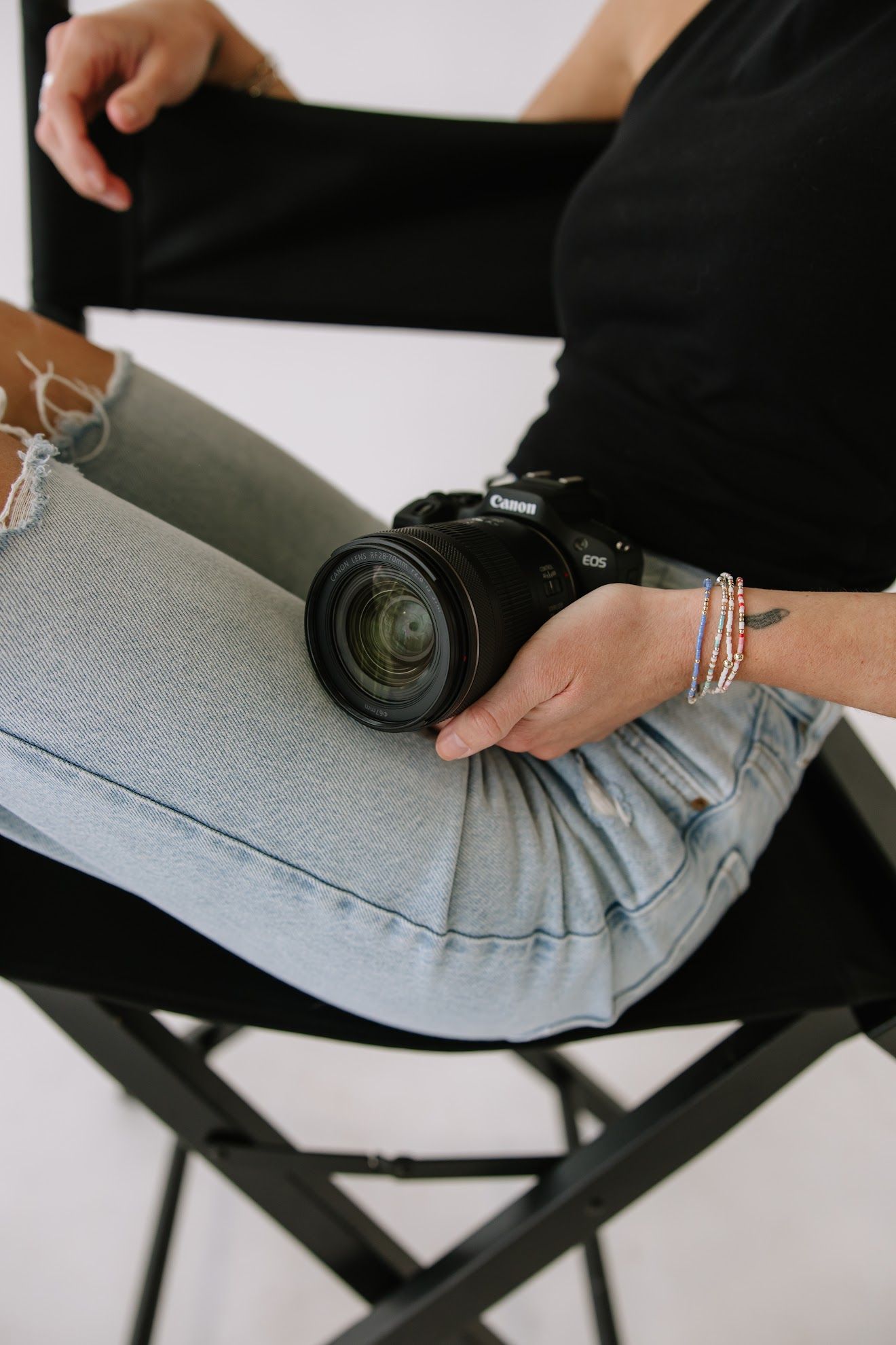 Person in black top and jeans holding Canon DSLR camera on lap.