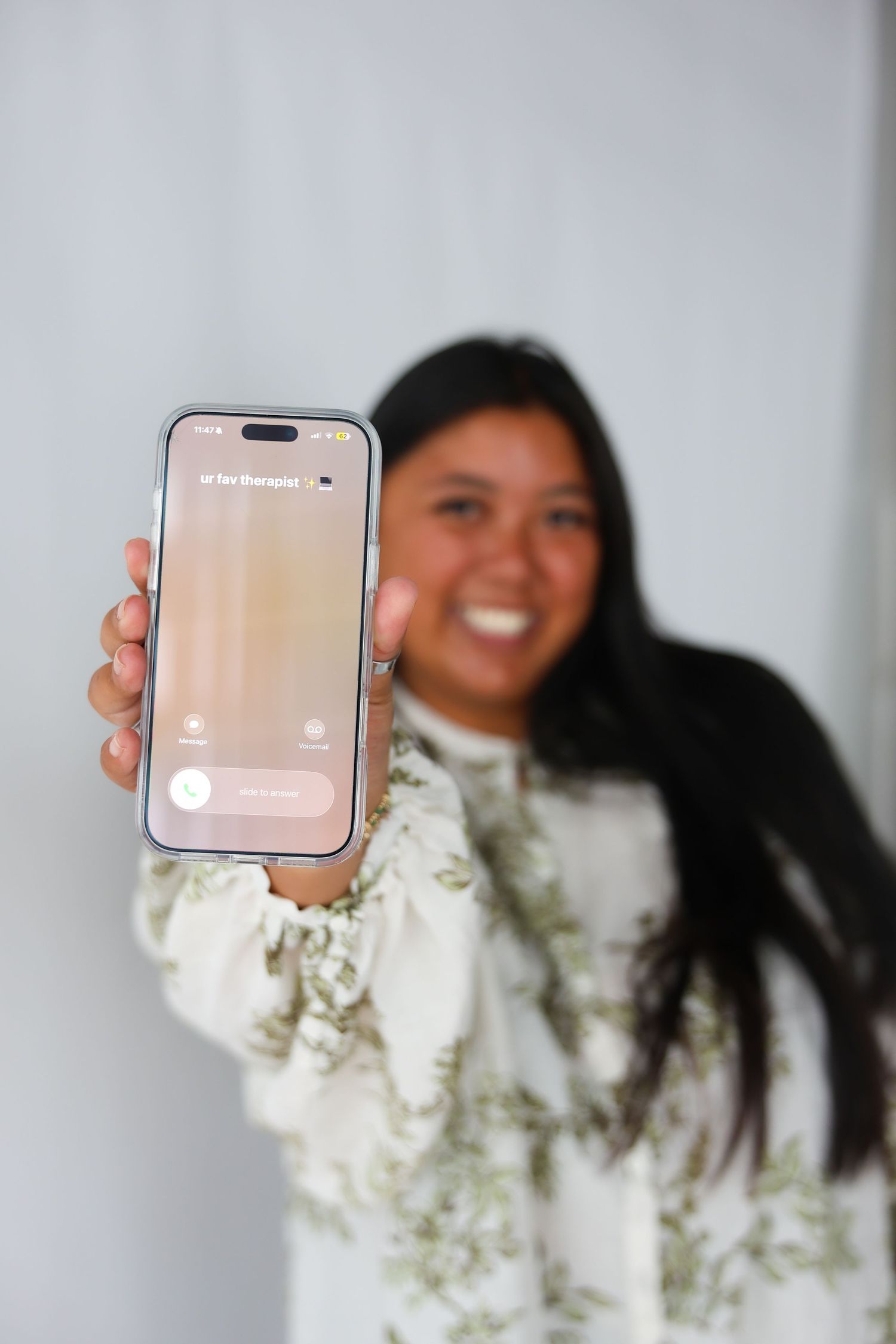 Smiling young woman holding up an iPhone displaying an incoming call screen toward the camera.