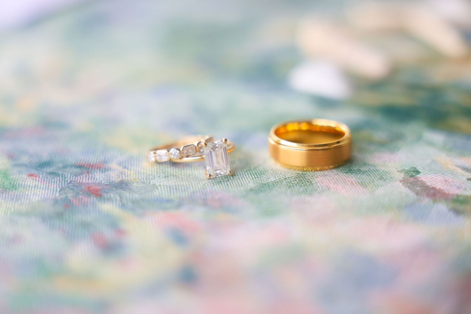 Diamond engagement ring and gold wedding band resting on a floral surface, perfect for wedding jewelry inspiration.