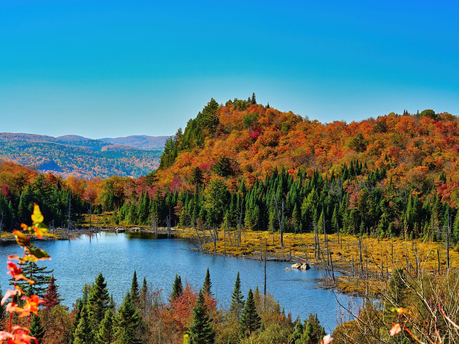 Autumn colors paint the landscape around a serene lake surrounded by mountains and forests.