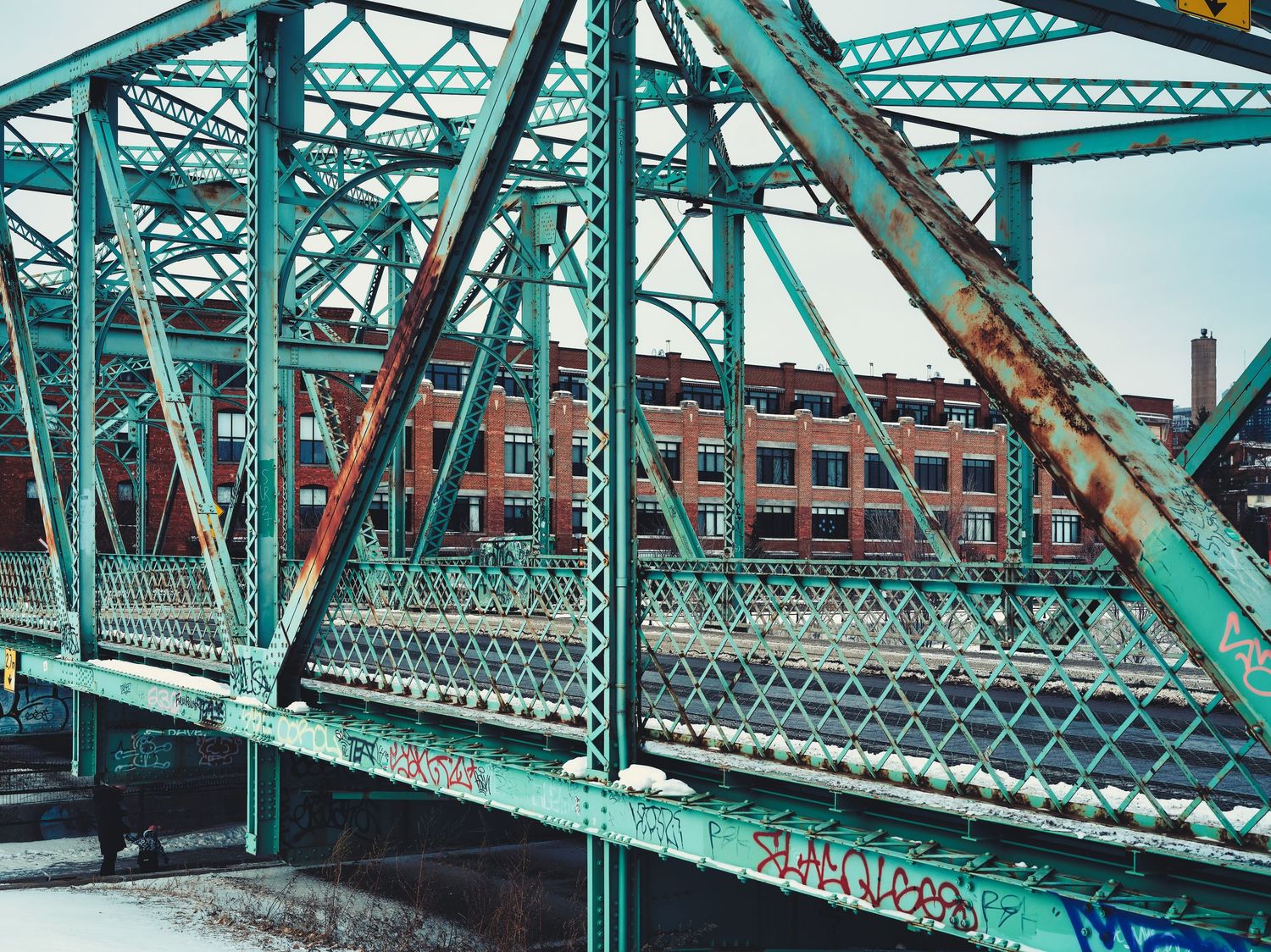 Turquoise steel bridge structure with intricate lattice work spanning across water.