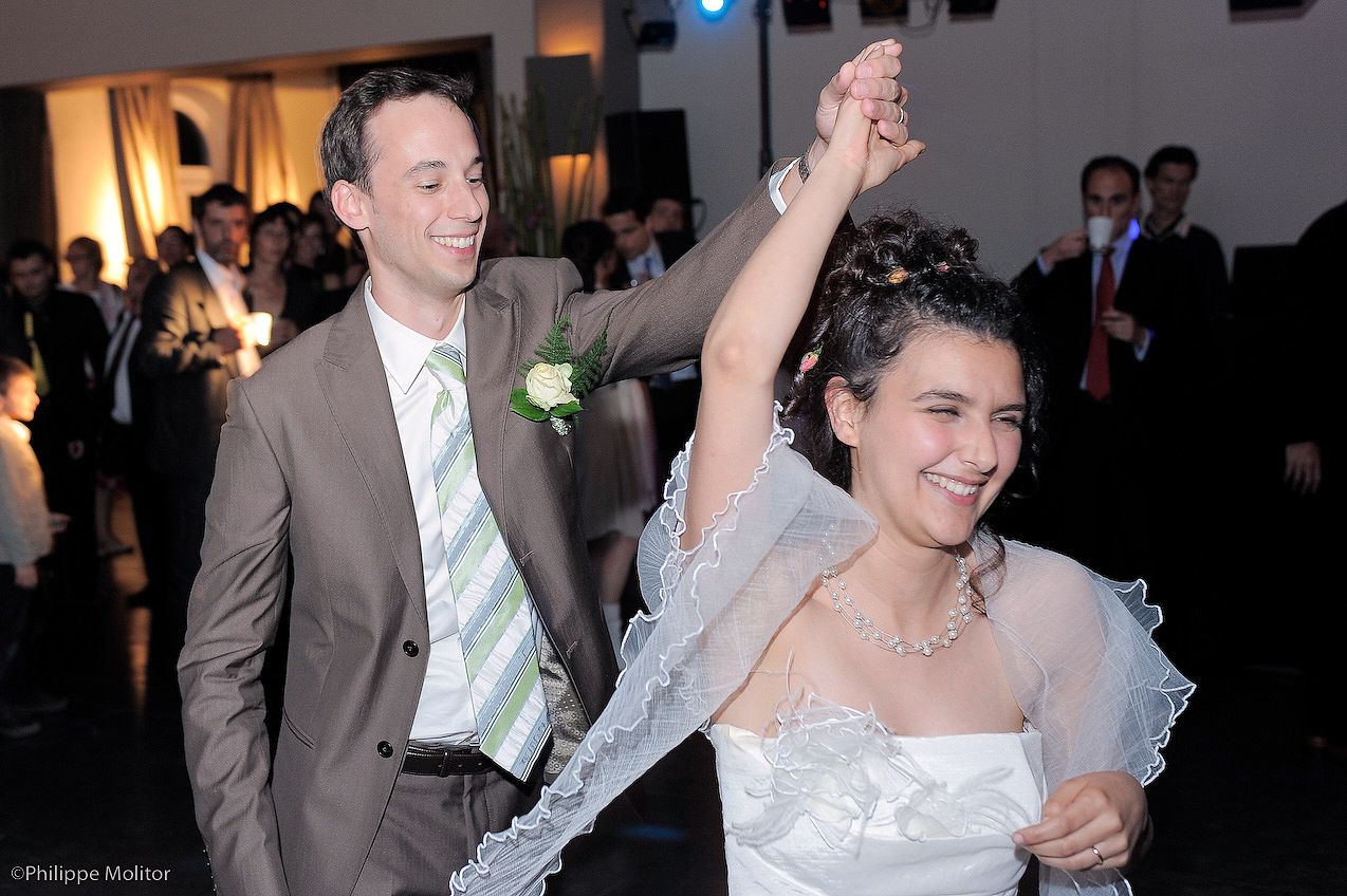Bride and groom dancing joyfully at their wedding reception, with guests celebrating in the background.