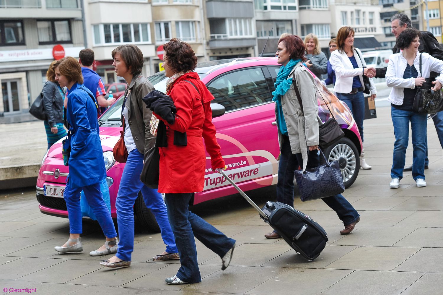 People walking in a line outside a building with parked cars.