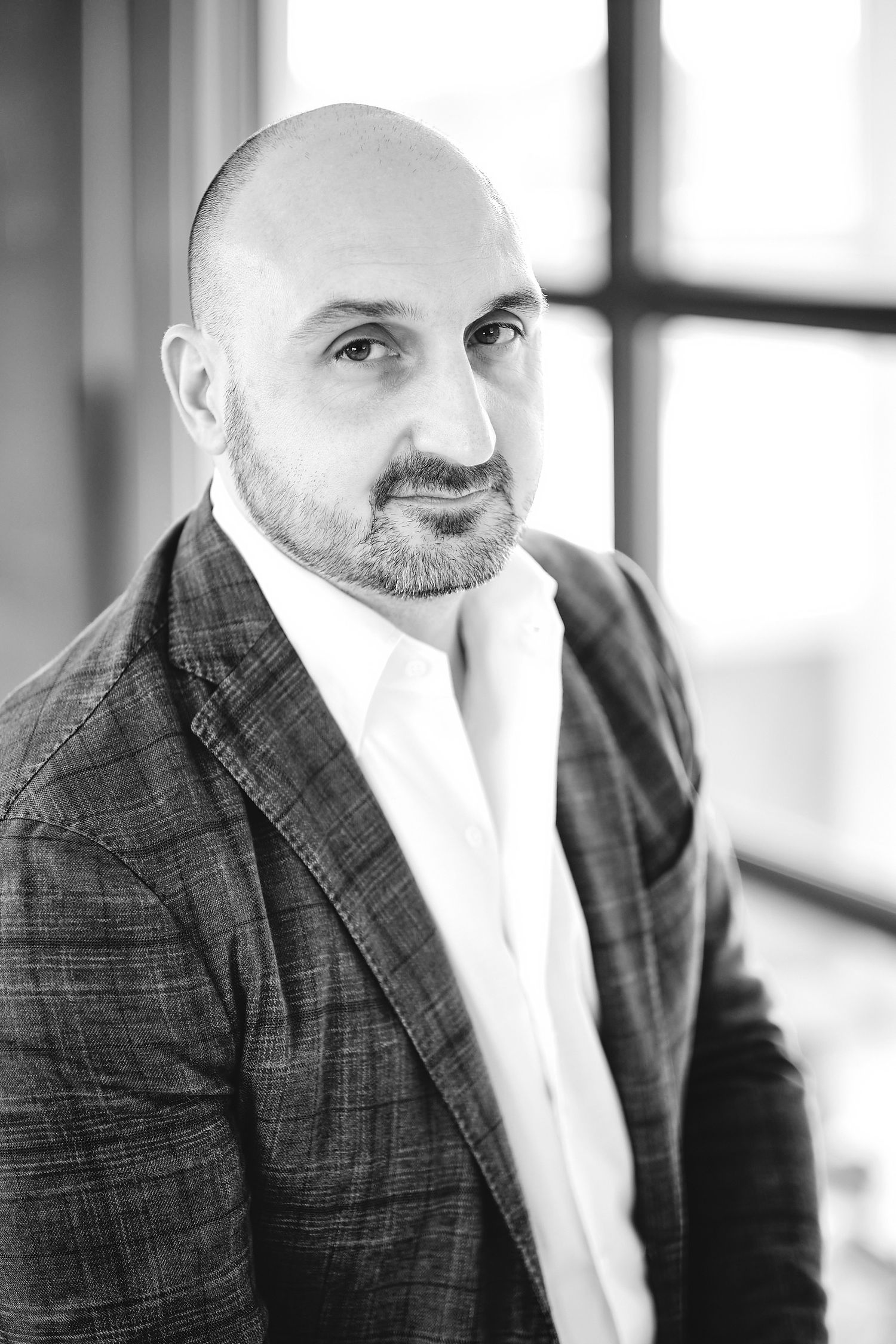 Business portrait series in plaid suit jacket and white shirt against window lighting.