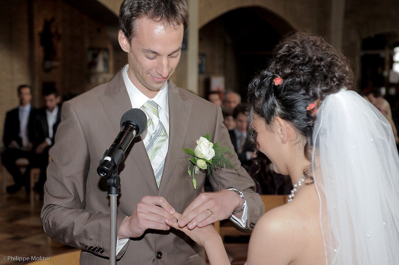 Groom places wedding ring on brides finger at altar during church ceremony with microphone stand nearby.