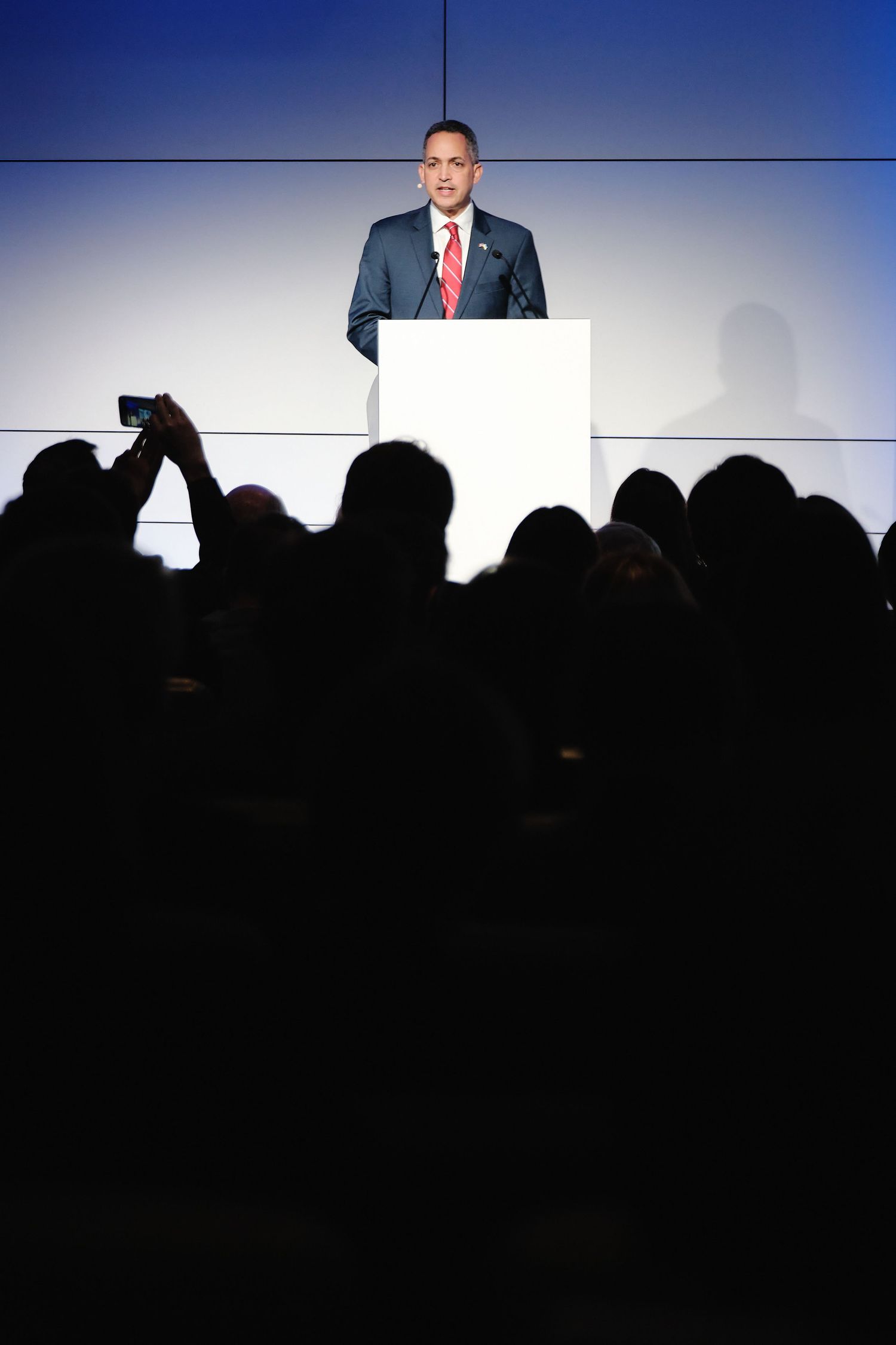 Speaker addressing audience at conference with silhouetted crowd in foreground.