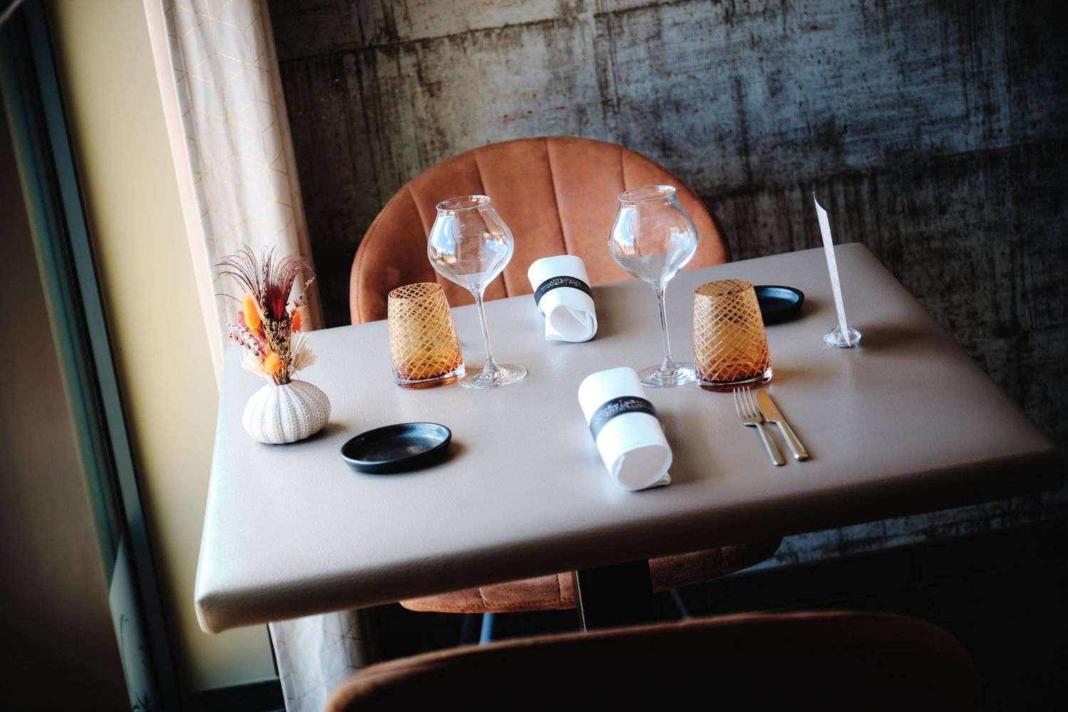Intimate dining area with white tablecloths and warm lighting against textured concrete walls.