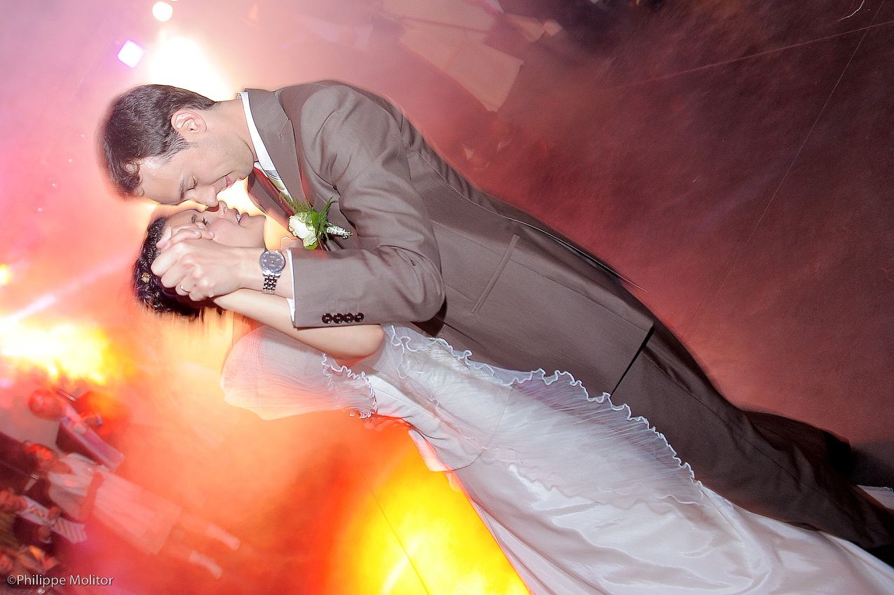 Bride and groom share a romantic dip kiss on the dance floor surrounded by colorful lights.