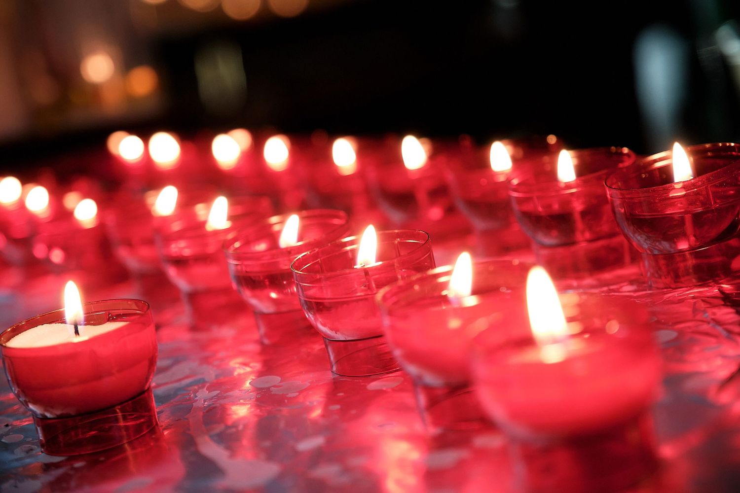 Rows of glowing red votive candles in glass holders creating a warm, atmospheric display.
