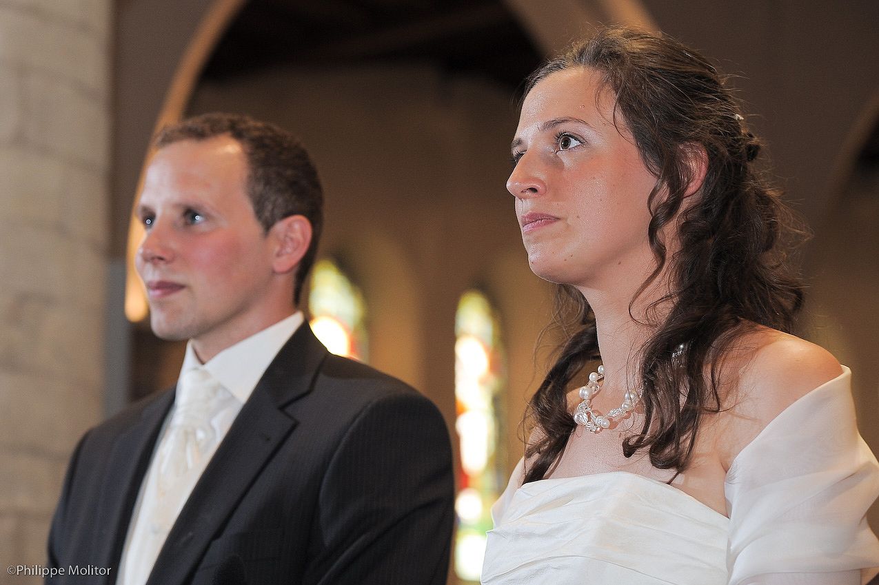 A bride and groom stand together in a church during their wedding ceremony, both gazing forward with joyful expressions.