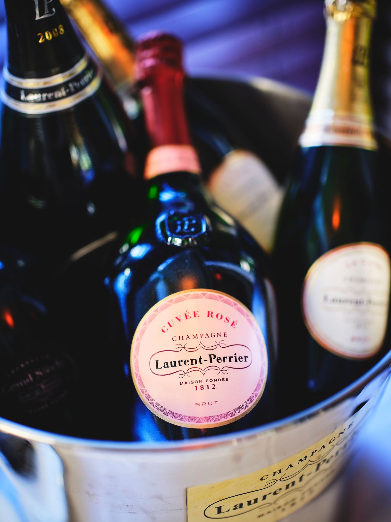 Collection of luxury champagne bottles including Laurent-Perrier displayed with dramatic blue lighting.