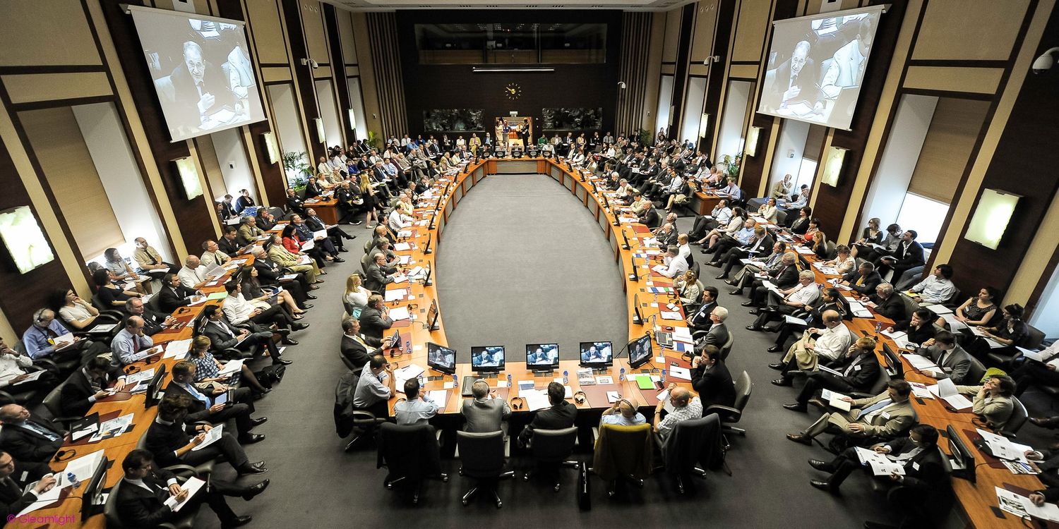 Wide angle view of large conference hall filled with attendees in rows of seating.
