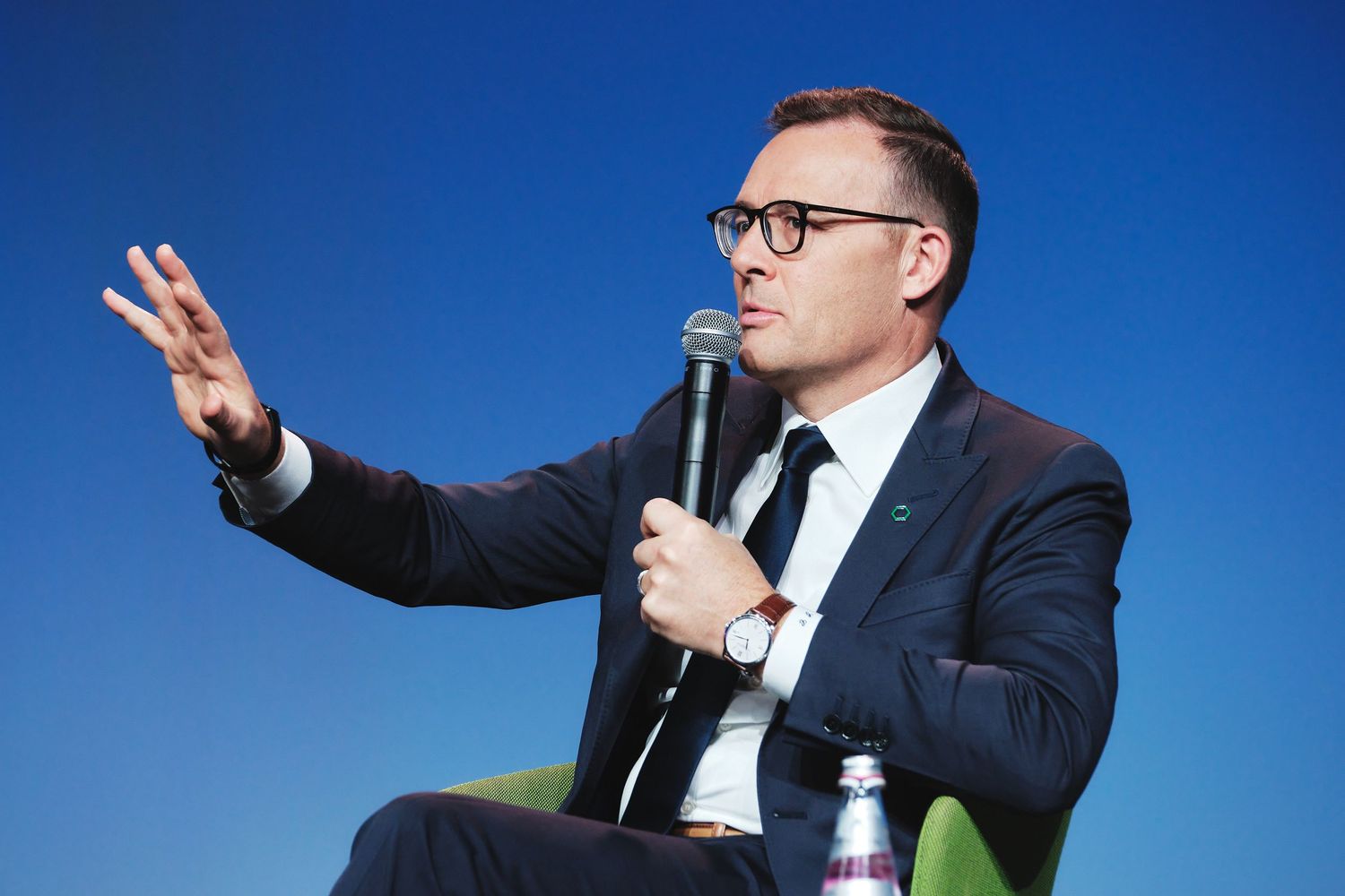Professional speaker gestures animatedly while presenting on stage against blue backdrop.