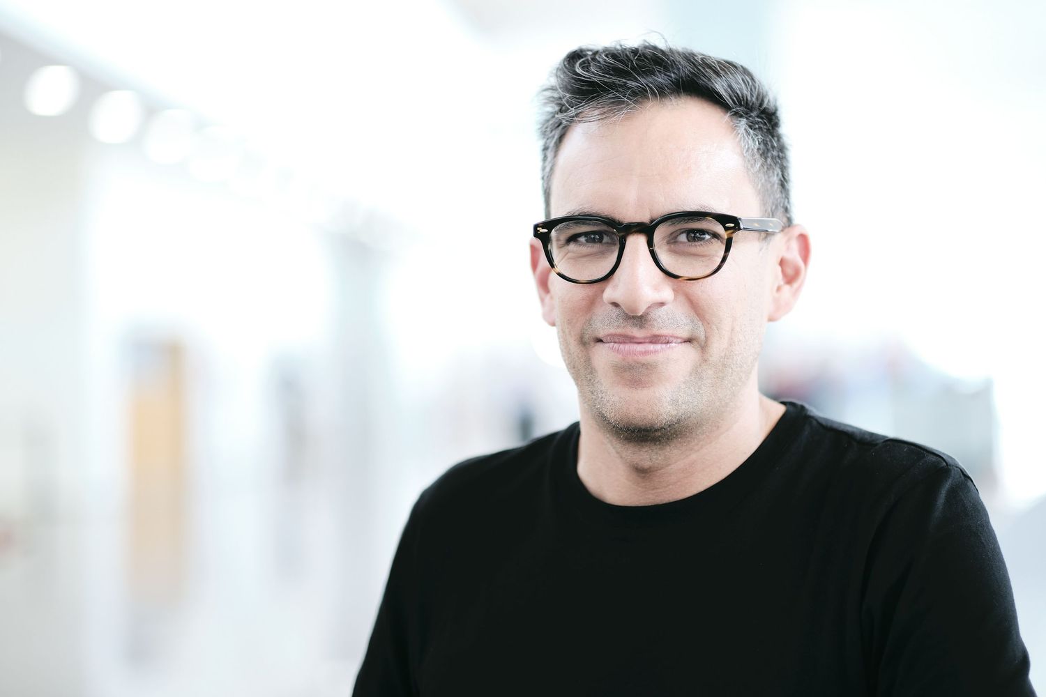 Professional portrait of person wearing glasses in bright office setting.