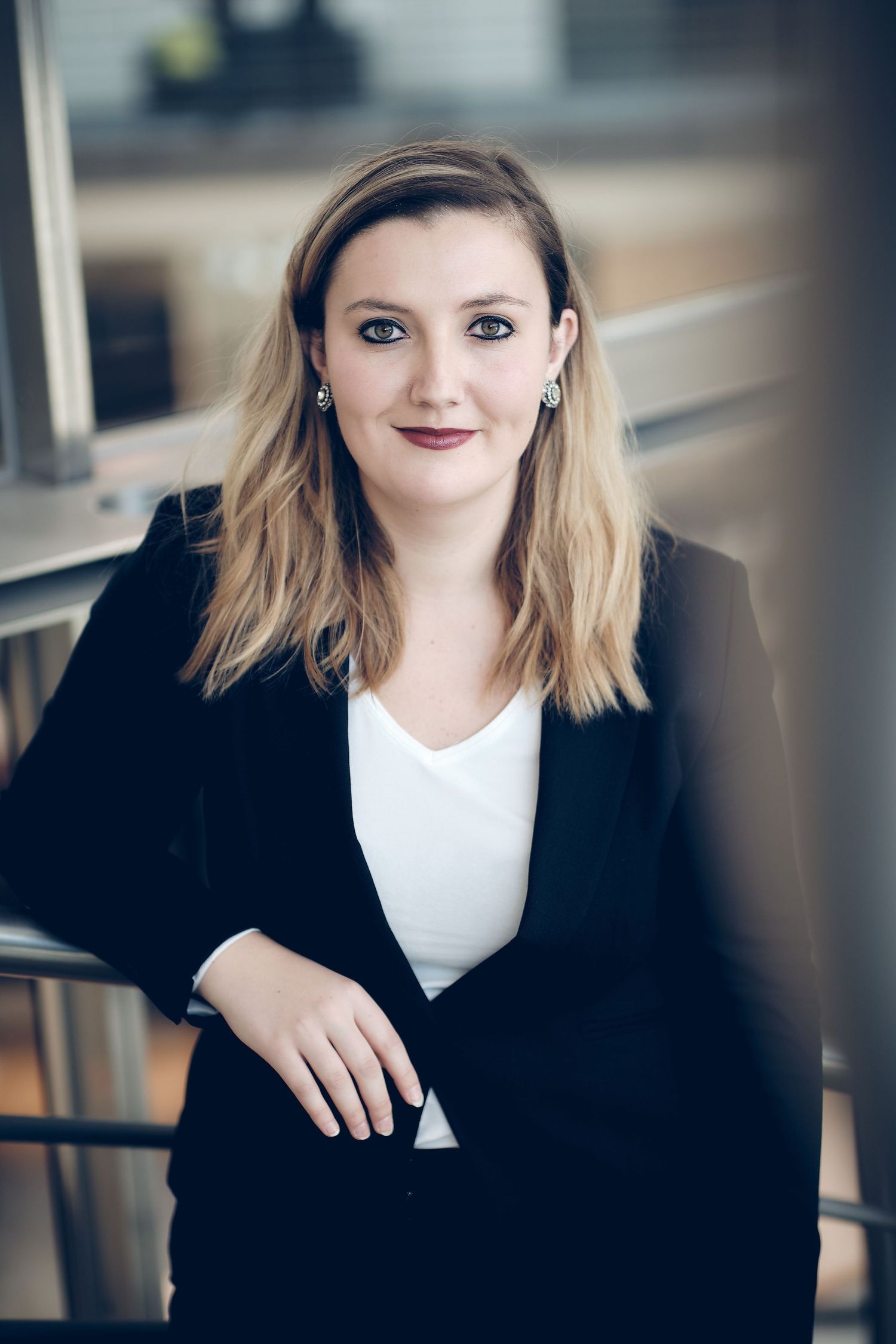 Professional headshots of person in black blazer and white top against office background.