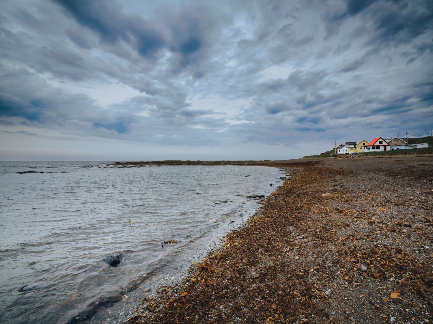 Dramatic cloudy sky over a rocky coastline with waves crashing against the shore.
