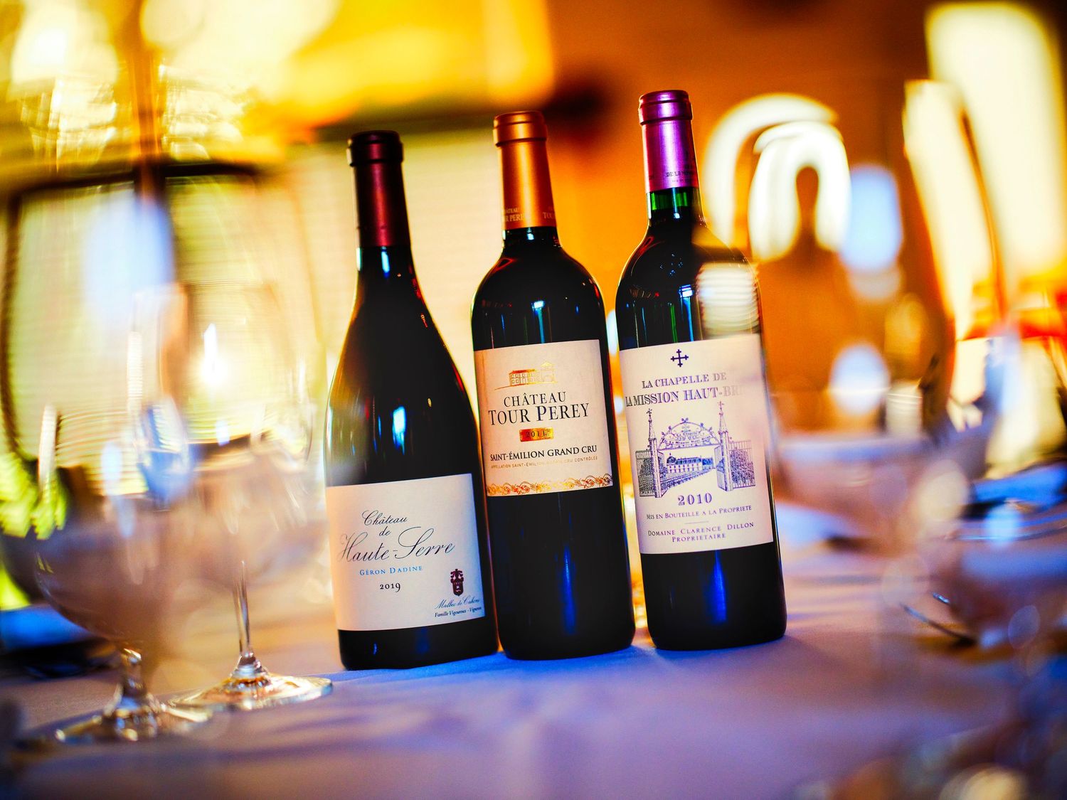 Wine bottles lined up on a bar counter with warm ambient lighting creating a bokeh effect in the background.