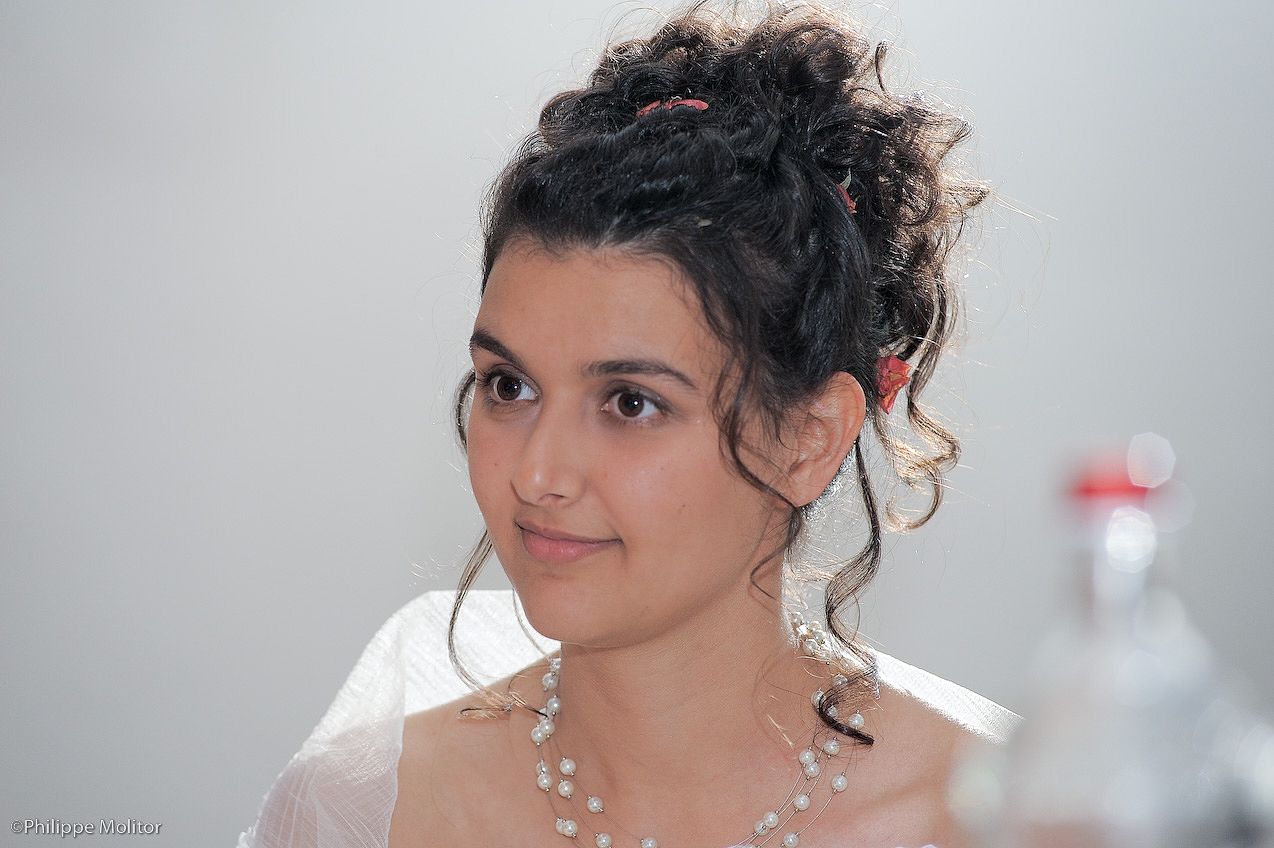Young bride with elegant updo hairstyle, pearl necklace, and veil, smiling softly in a portrait photo.