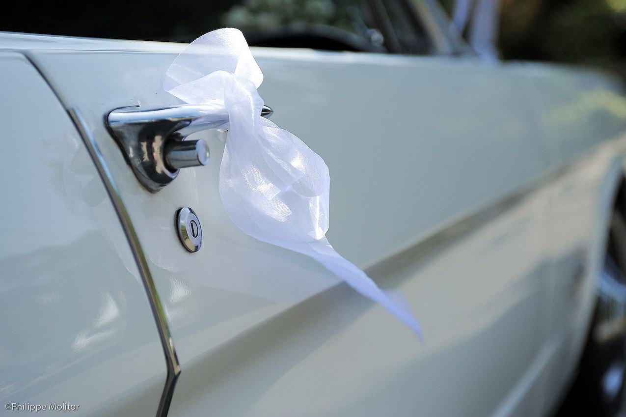 White ribbon bow decorating the door handle of a classic cream wedding car.