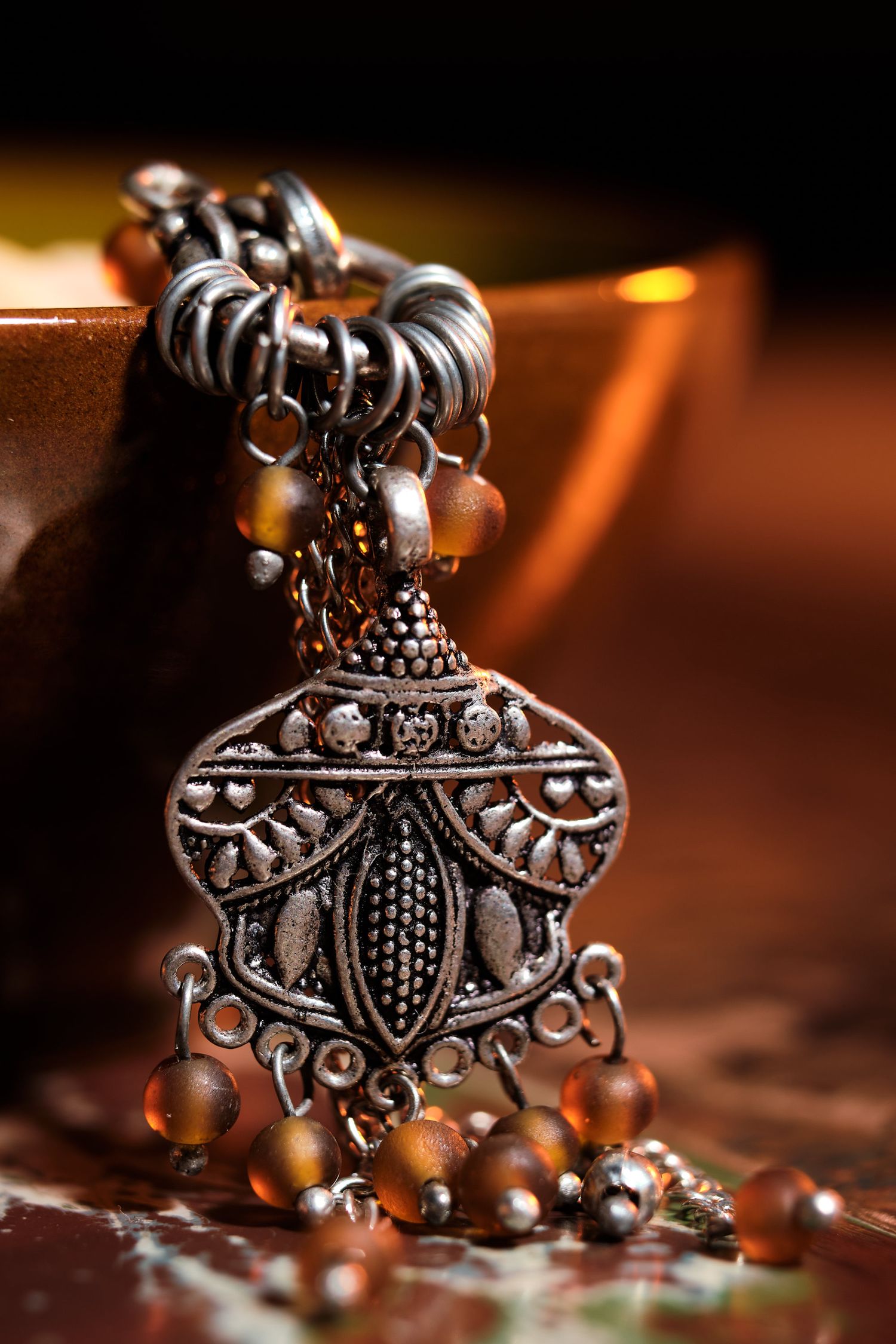 Ornate silver pendant with intricate filigree design photographed in warm lighting.