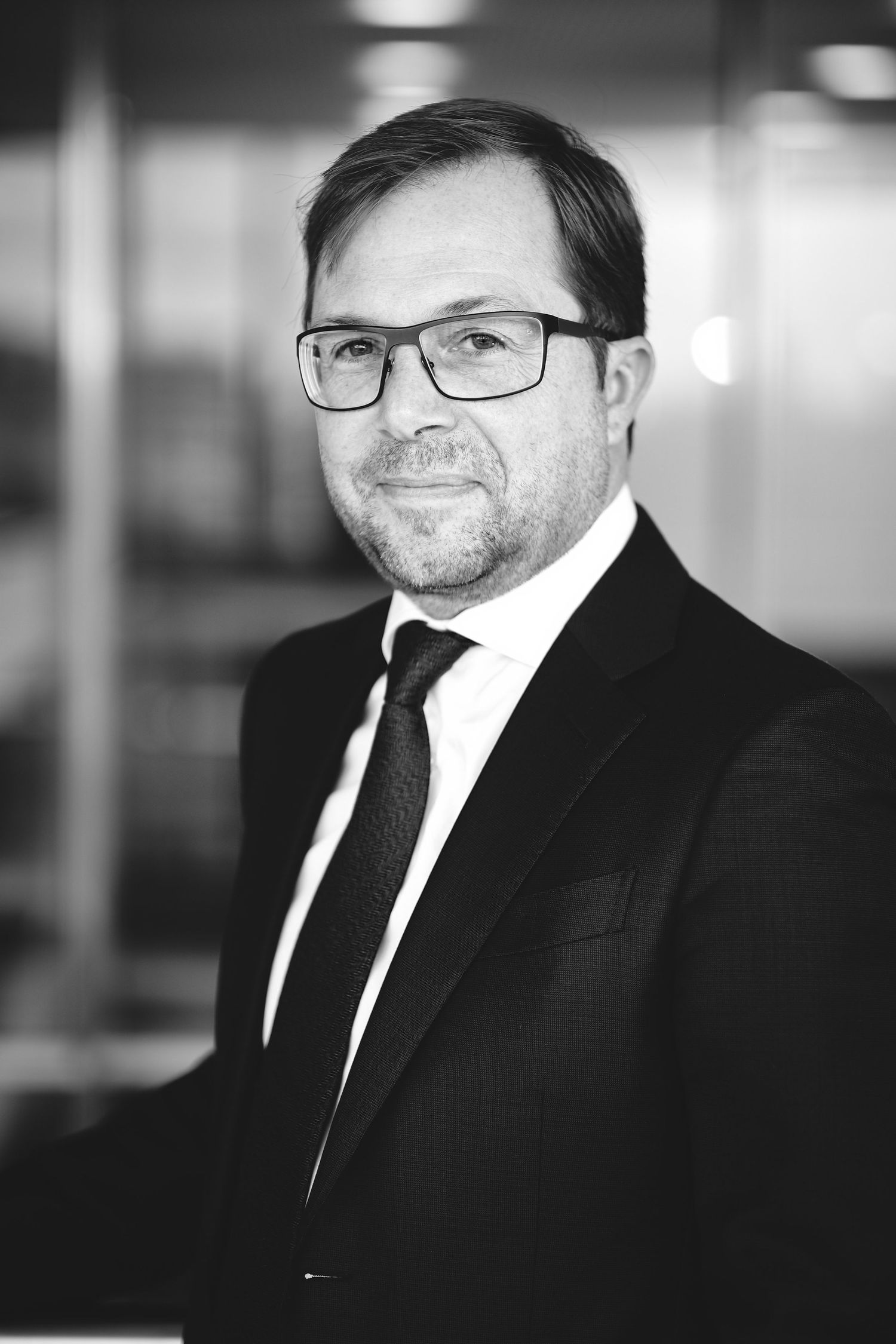Black and white corporate headshots of businessman wearing glasses and suit.
